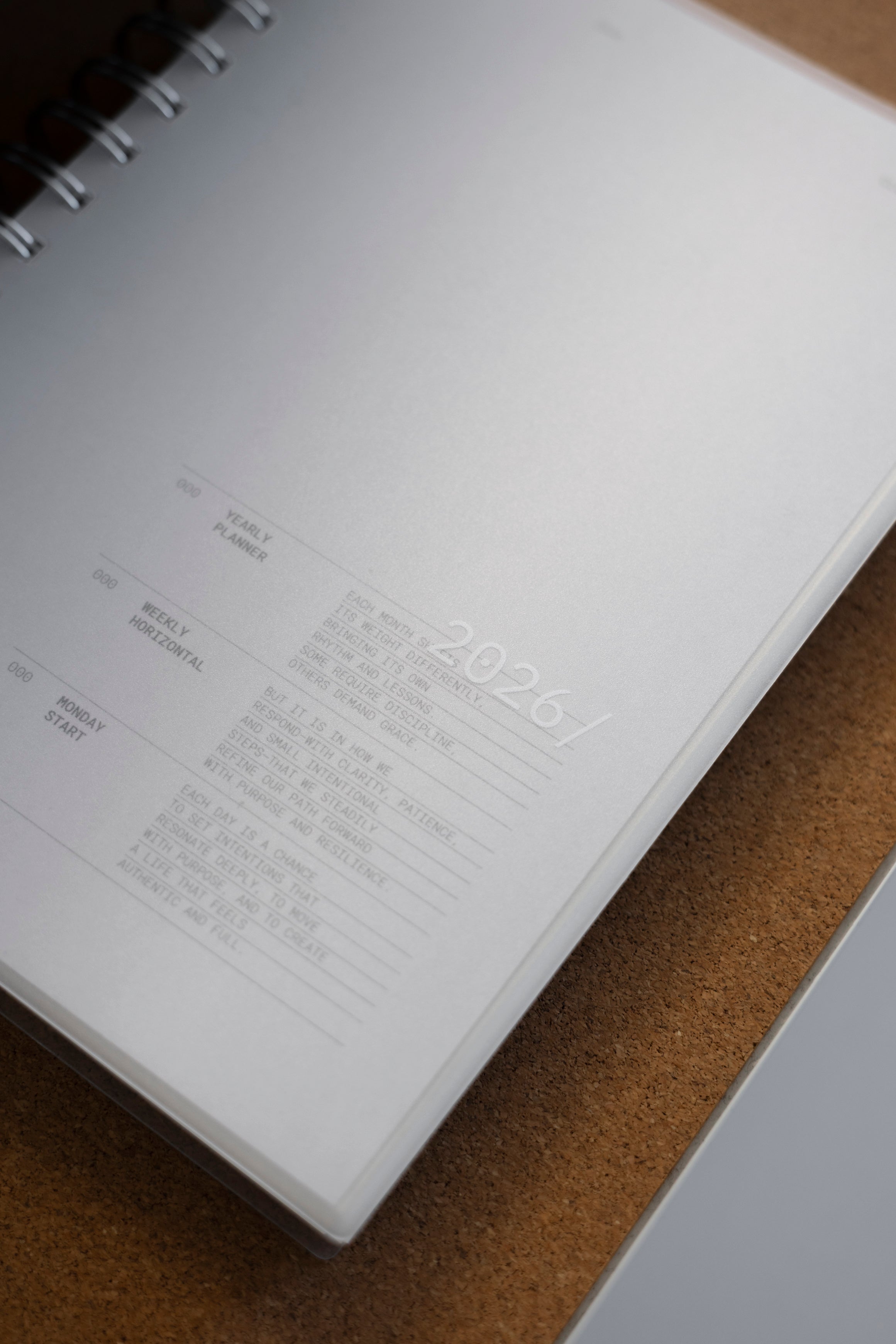 2026 Weekly Horizontal Notebook | Monday Start | A5 Spiral shown closed from the front laying down on a corkboard background. Features the clear plastic cover with '2026/' text.