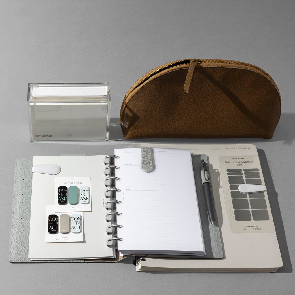 An Heirloom Leather Folio is opened to a page within an assembled discbound planner system.  There are other surrounding planner accessories including stickers, clips, pens, and more.