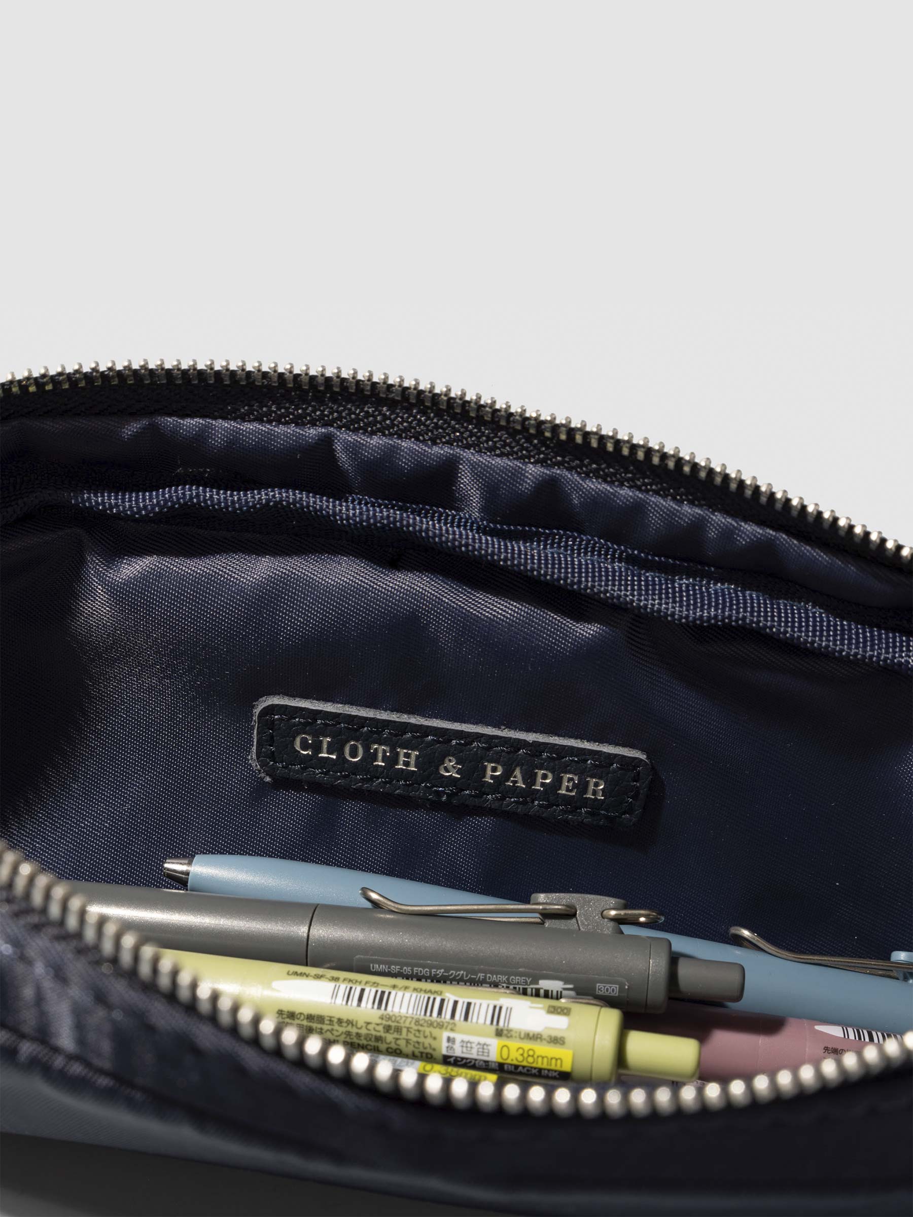 Closeup of Cloth and Paper logo inside of pencil pouch. A selection of pens are stored inside the pouch. Color featured is Apollo.