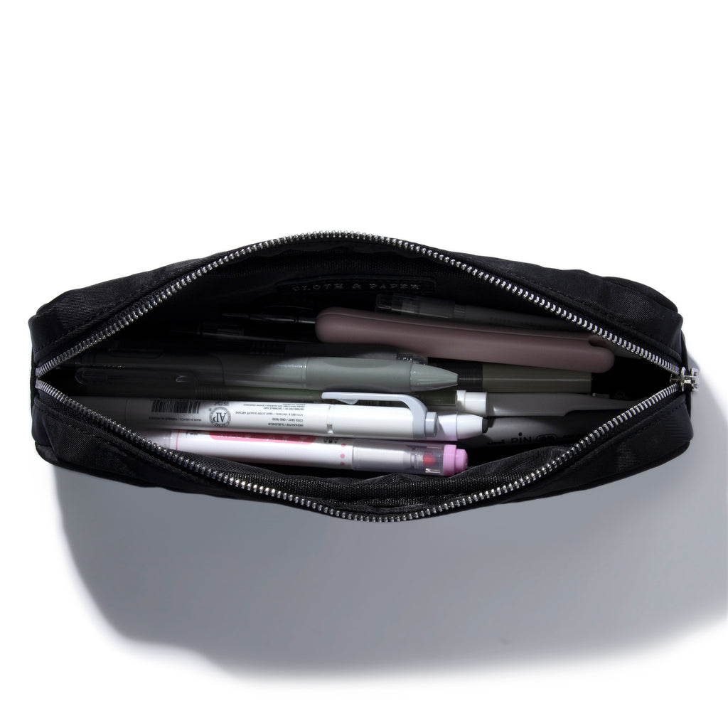 Pencil pouch displayed unzipped with a collection of pens and accessories stored inside. Color featured is black.