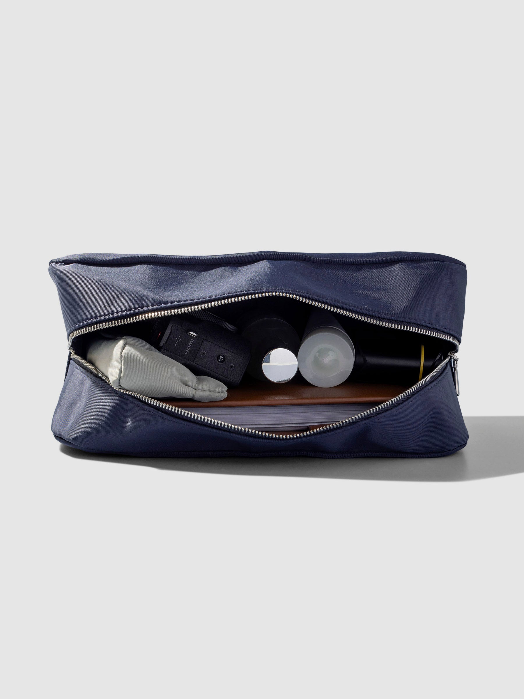 Pouch shown open from a top down angle, filled with a small pouch liner, digital camera, two small bottles, and a planner.