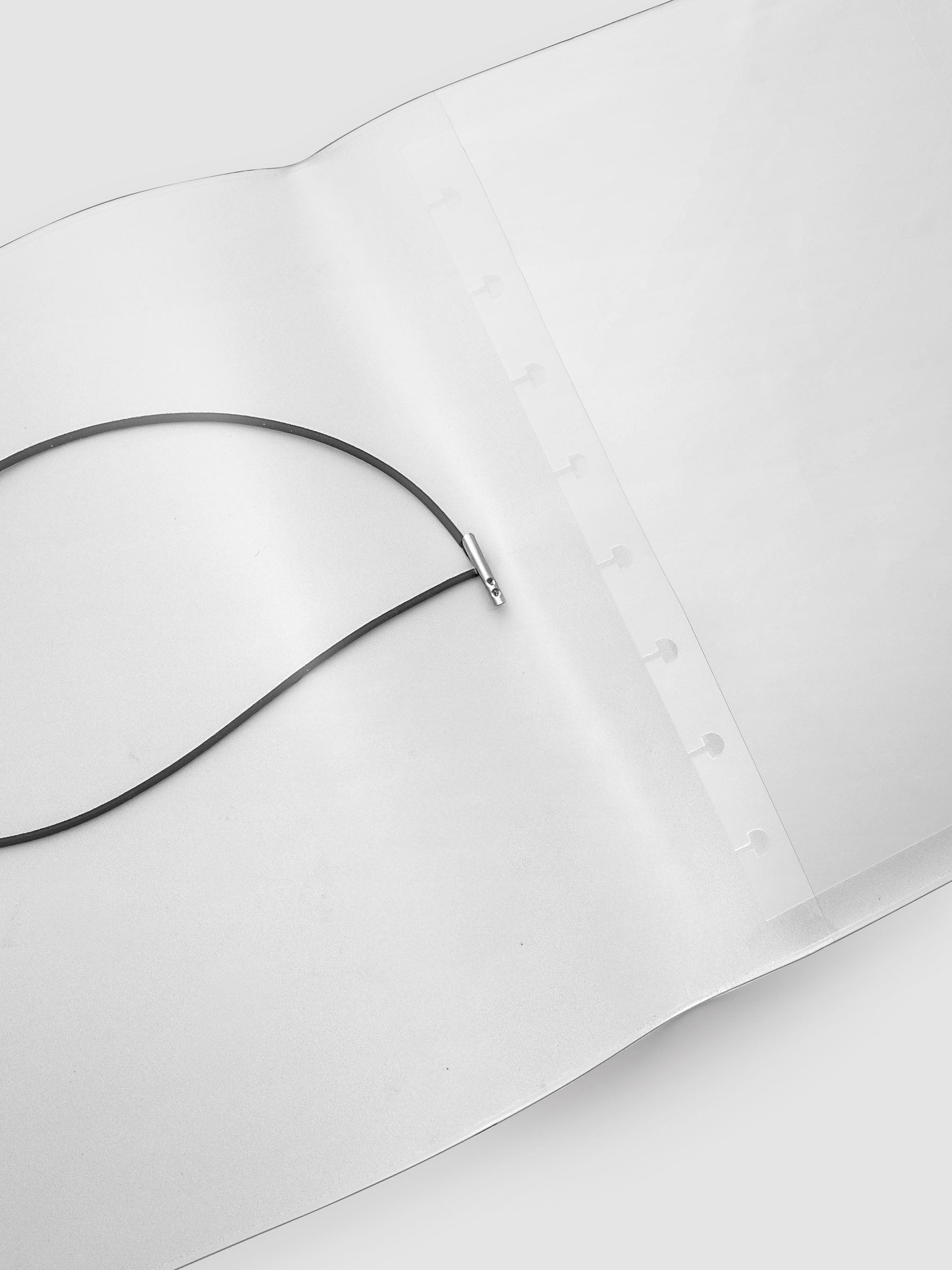 A clear plastic notebook cover with a black elastic closure band, opened and zoomed in to feature the black cord, against a light gray background.