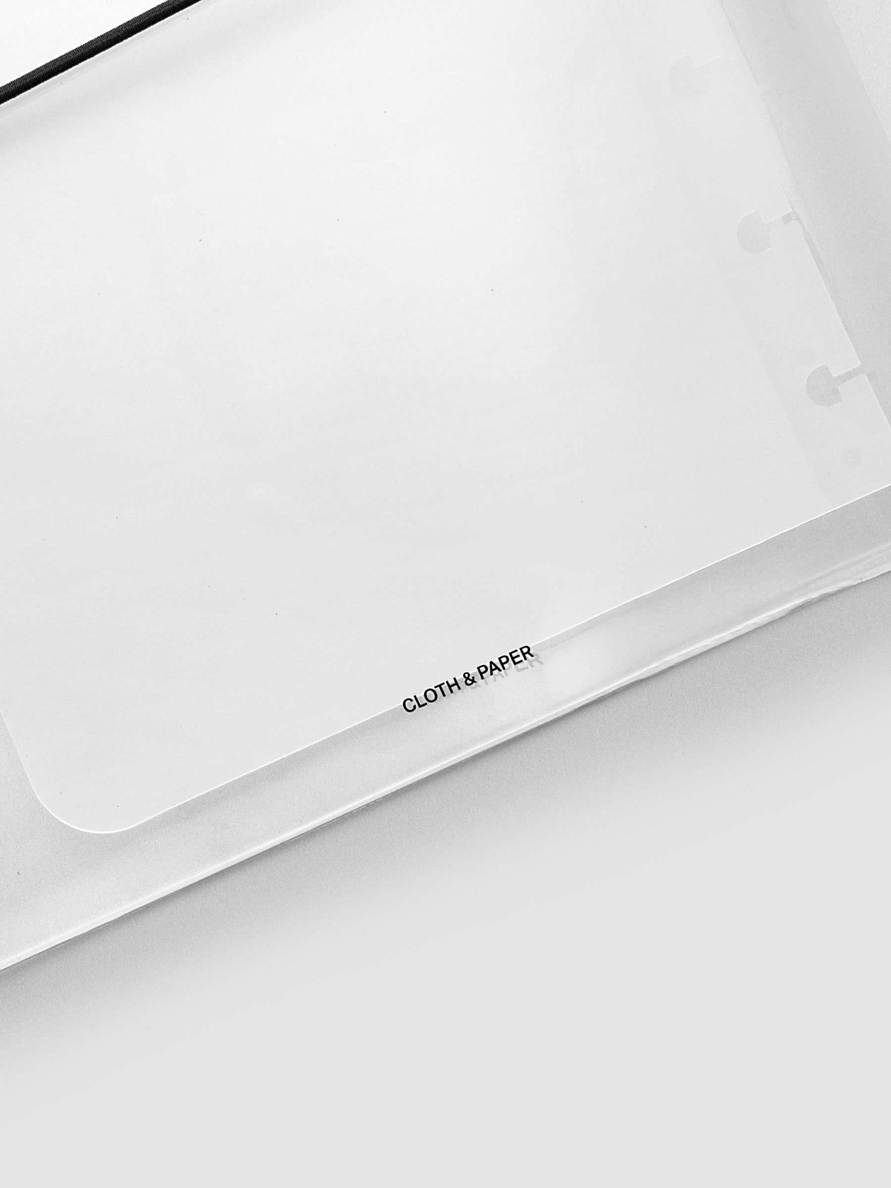 A clear plastic cover with a black elastic band closure, featuring the text 'CLOTH & PAPER' printed in black near the bottom, shot on a light gray background.