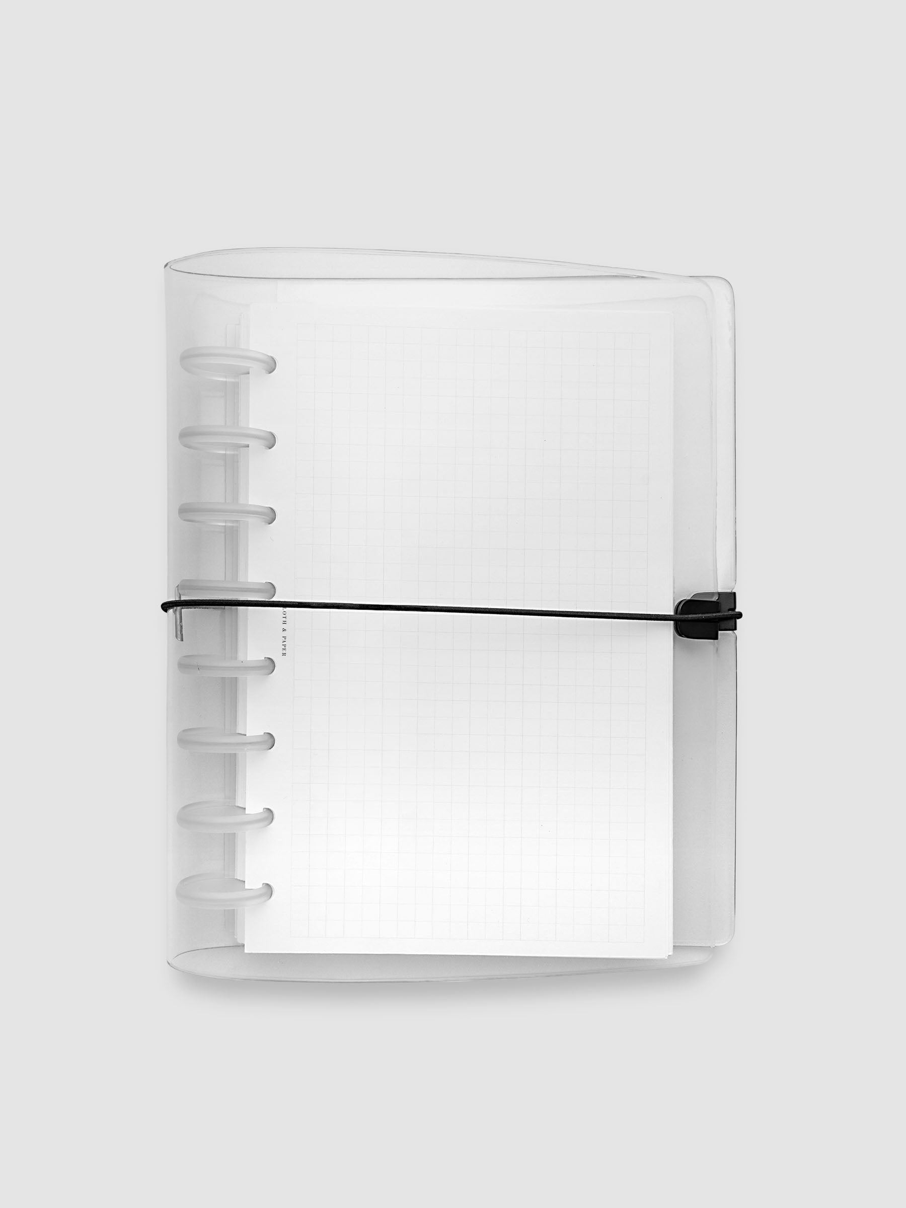 A clear plastic notebook cover with a black elastic closure band, with a discbound planner and grid inserts inside, against a light gray background.