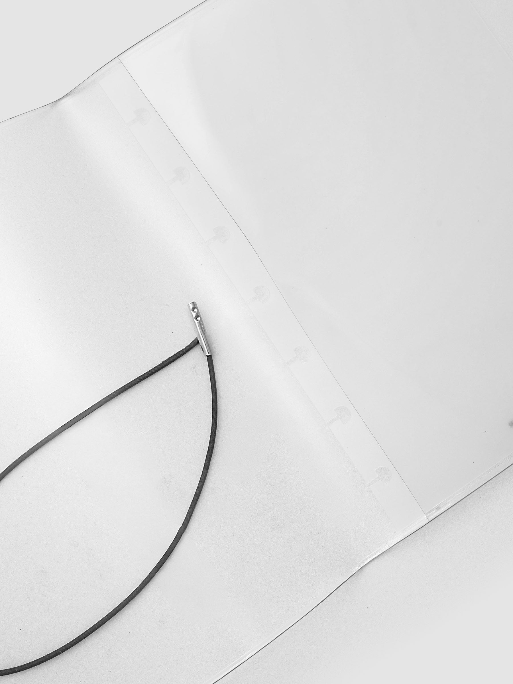 A close-up of a black cord or cable with a small silver metal connector, laid on a plain white surface.