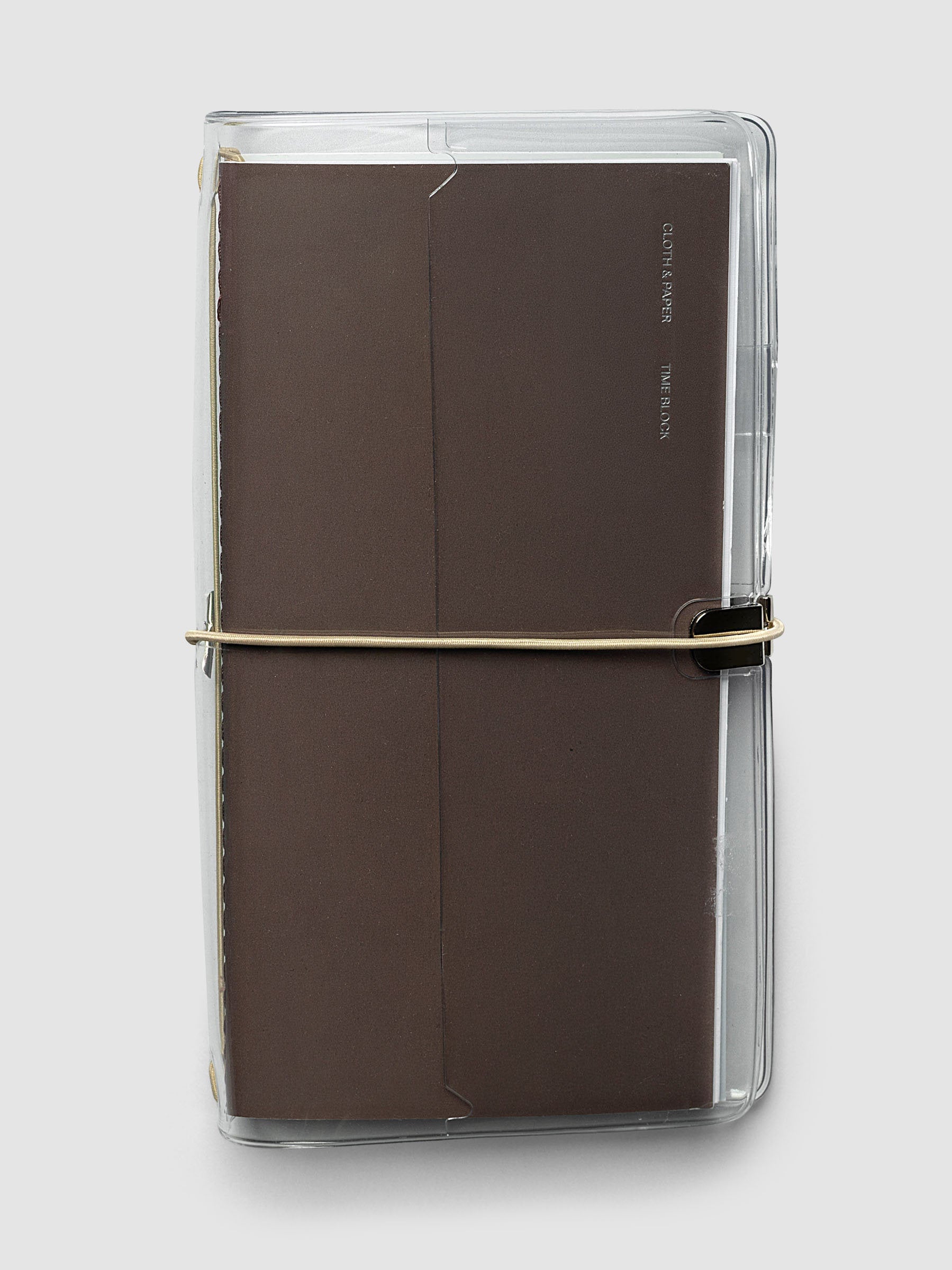 Clear Vinyl Travel Notebook Cover in A5 Slim shown closed with a brown travel notebook inside, secured with a beige bungee closure.