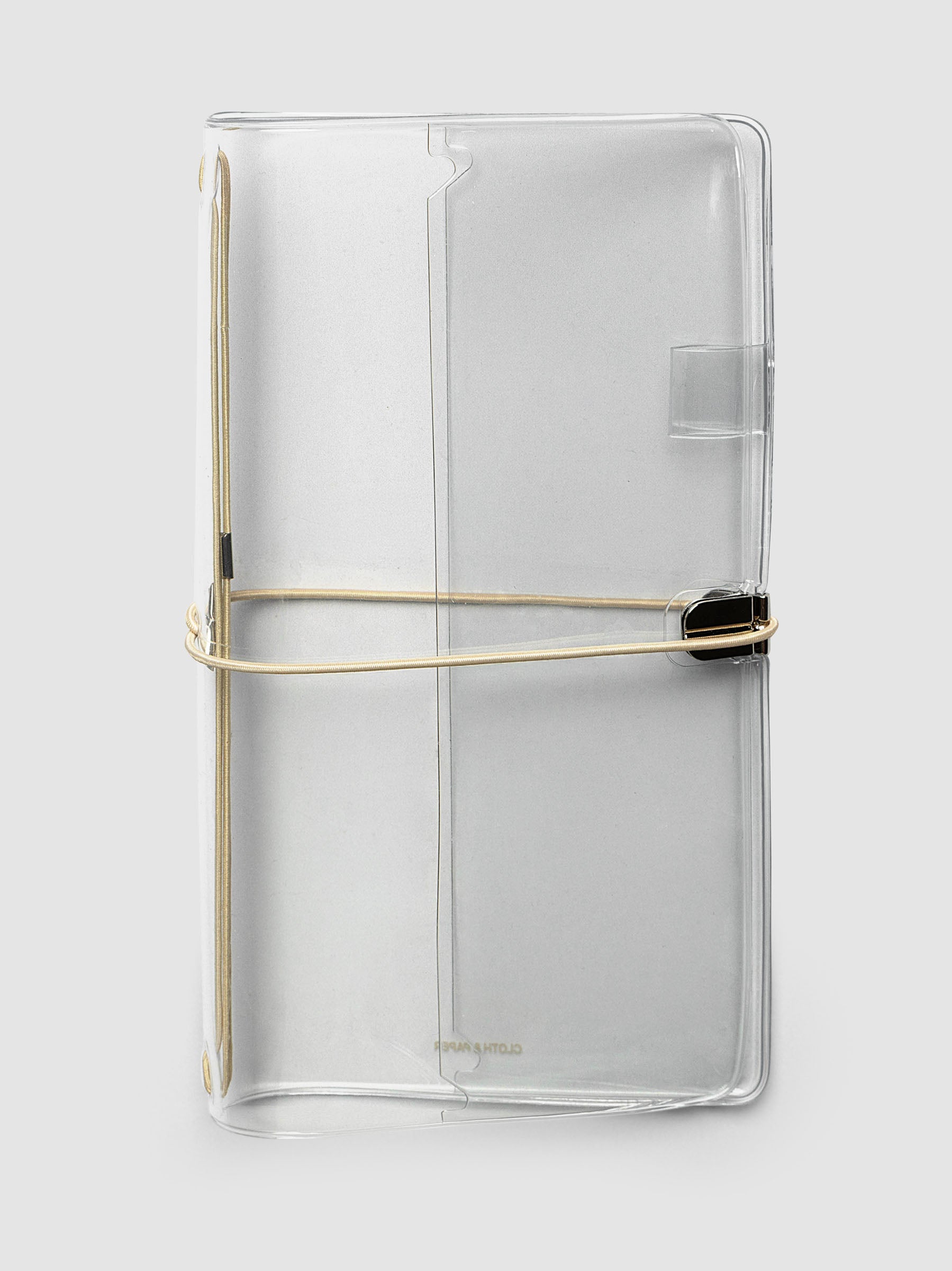 A clear acrylic notebook cover with a beige metal band closure, shown on a light gray background.