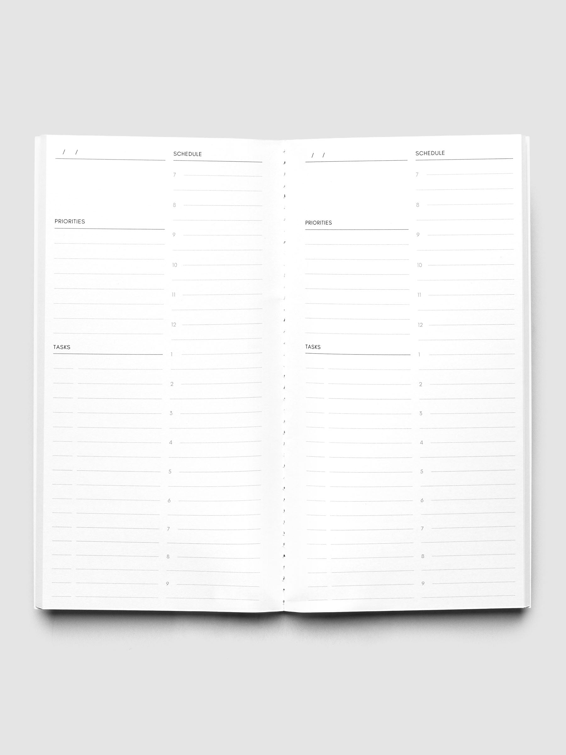 An open white daily planner or notebook showing lined sections for Monday through Sunday, with columns for priorities, tasks, and notes, photographed on a light gray background.