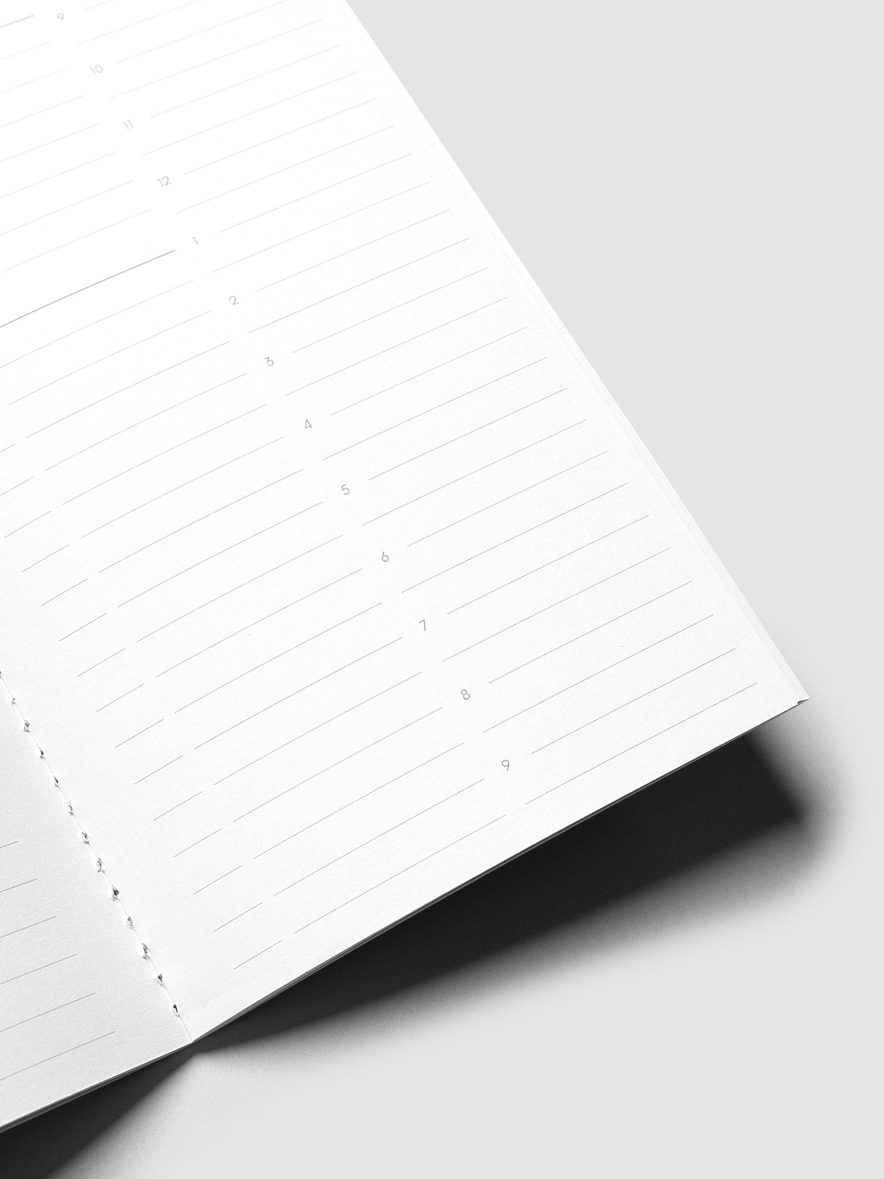 An open white lined notebook page photographed at an angle on a light gray background, with a dark shadow cast beneath the page.