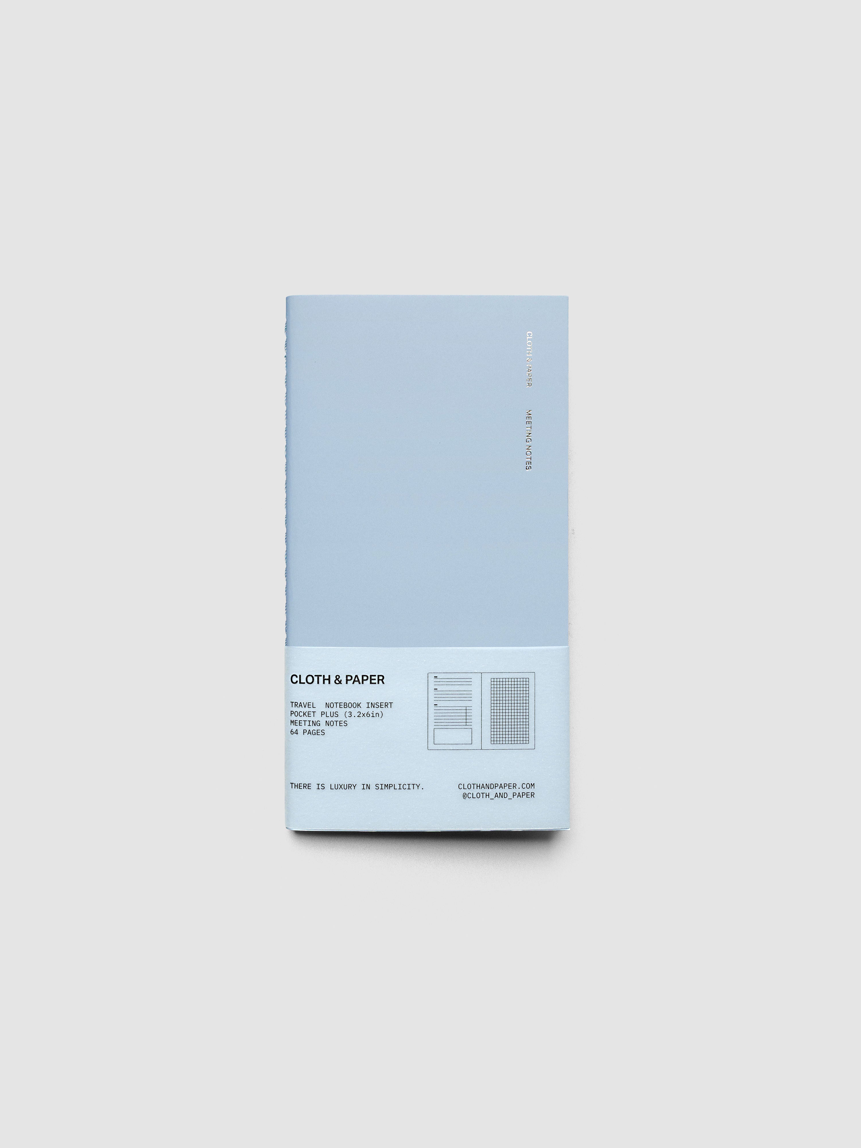 A light blue cloth and paper notebook with a vellum label at the bottom, shown on a neutral light gray background.