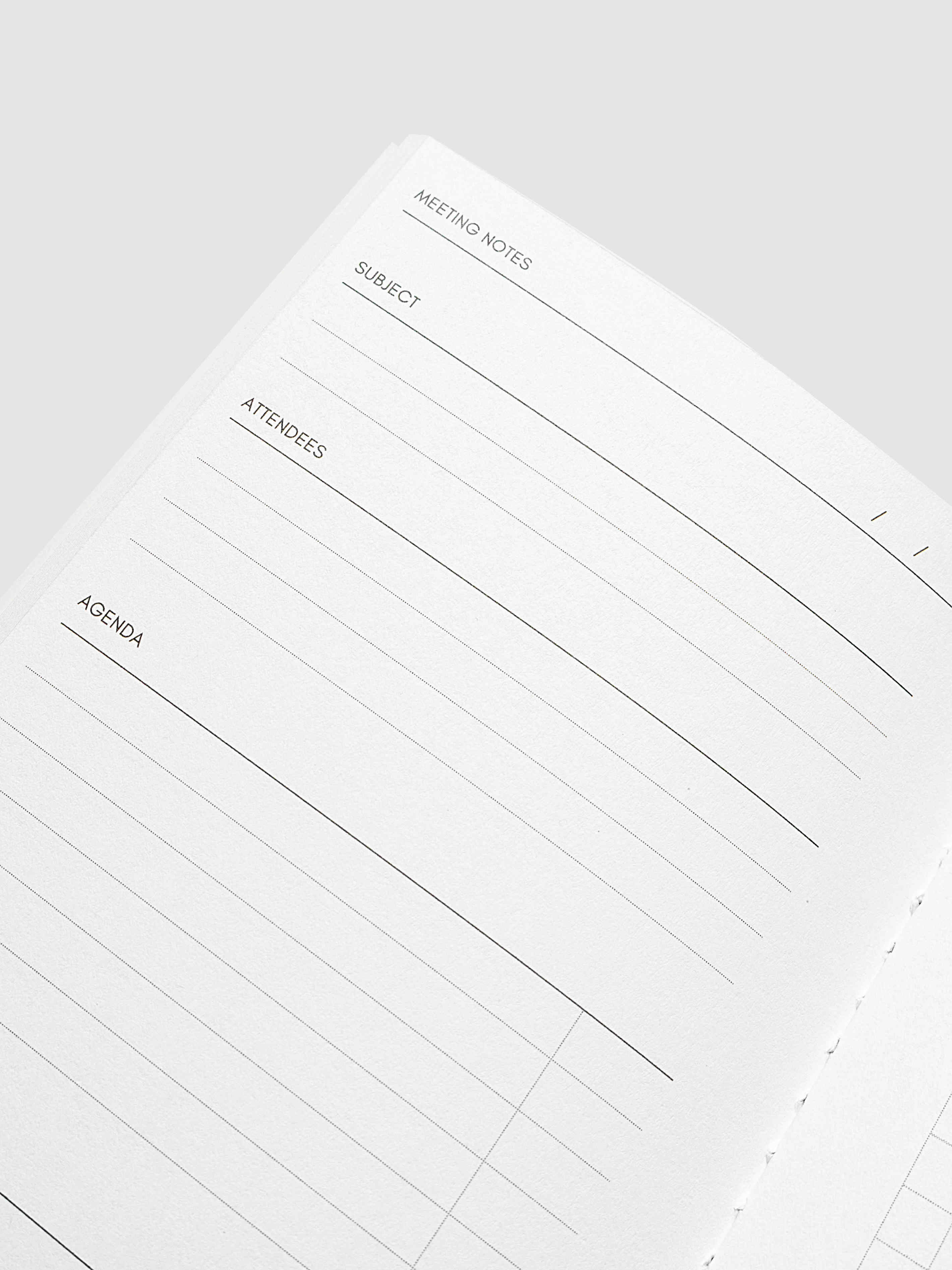 A close-up of an open planner or notebook page with lined meeting notes sections labeled Meeting Notes, Subject, Attendees, and Agenda on a light gray background.
