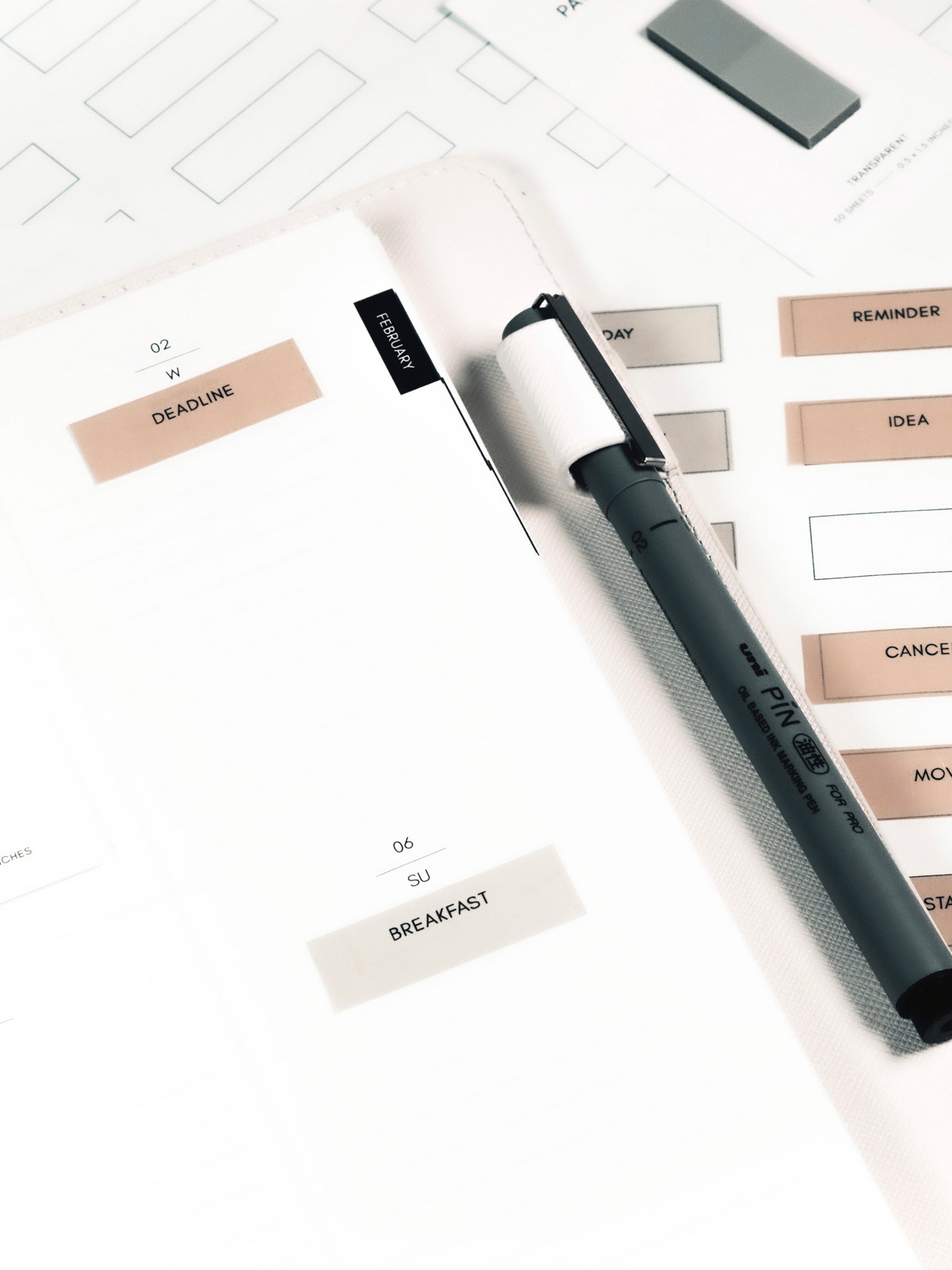 Close up on Page Flag Printable | Admin page flags in use inside a planner. The Uni Pin marking pen is in the planner's pen loop and a sheet of printed page flags are layered underneath the planner.