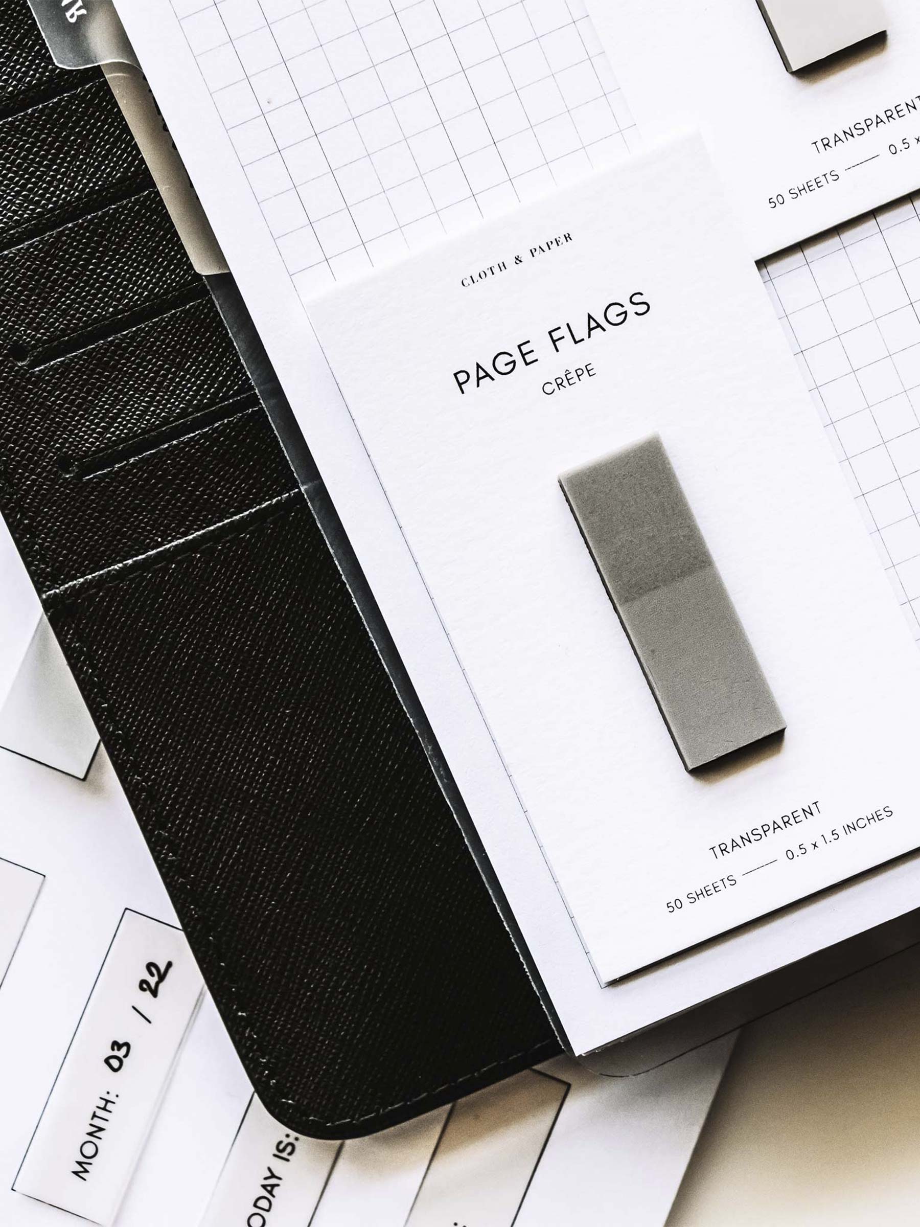 Close up on pad of page flags resting on the bottom left corner of a page in a planner. Underneath the planner is a page of printed page flags.