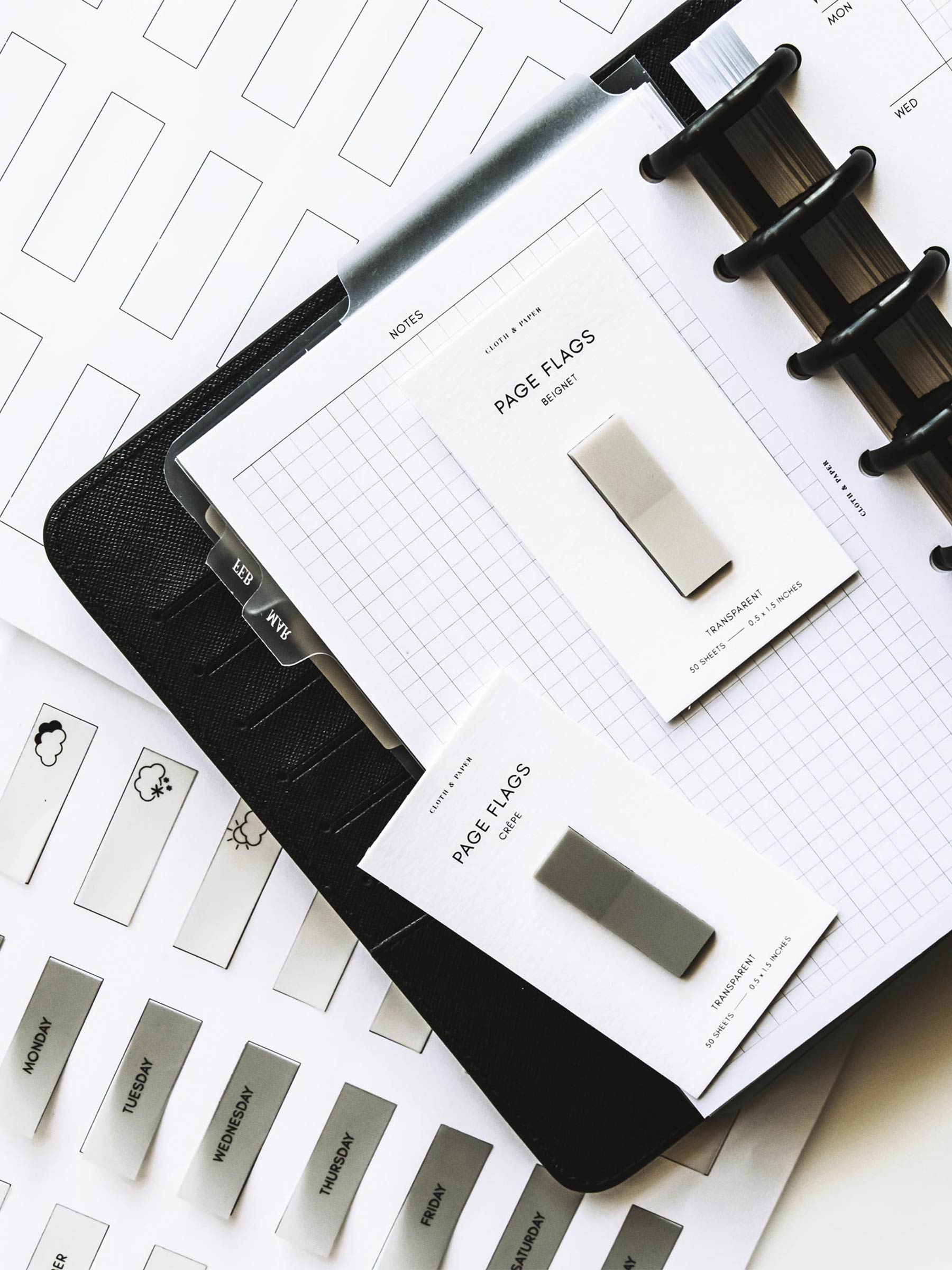 Printed page flags from Page Flag Printable in Essentials on a table next to an open discbound planner. There are two pads of page flags on top of the planner.