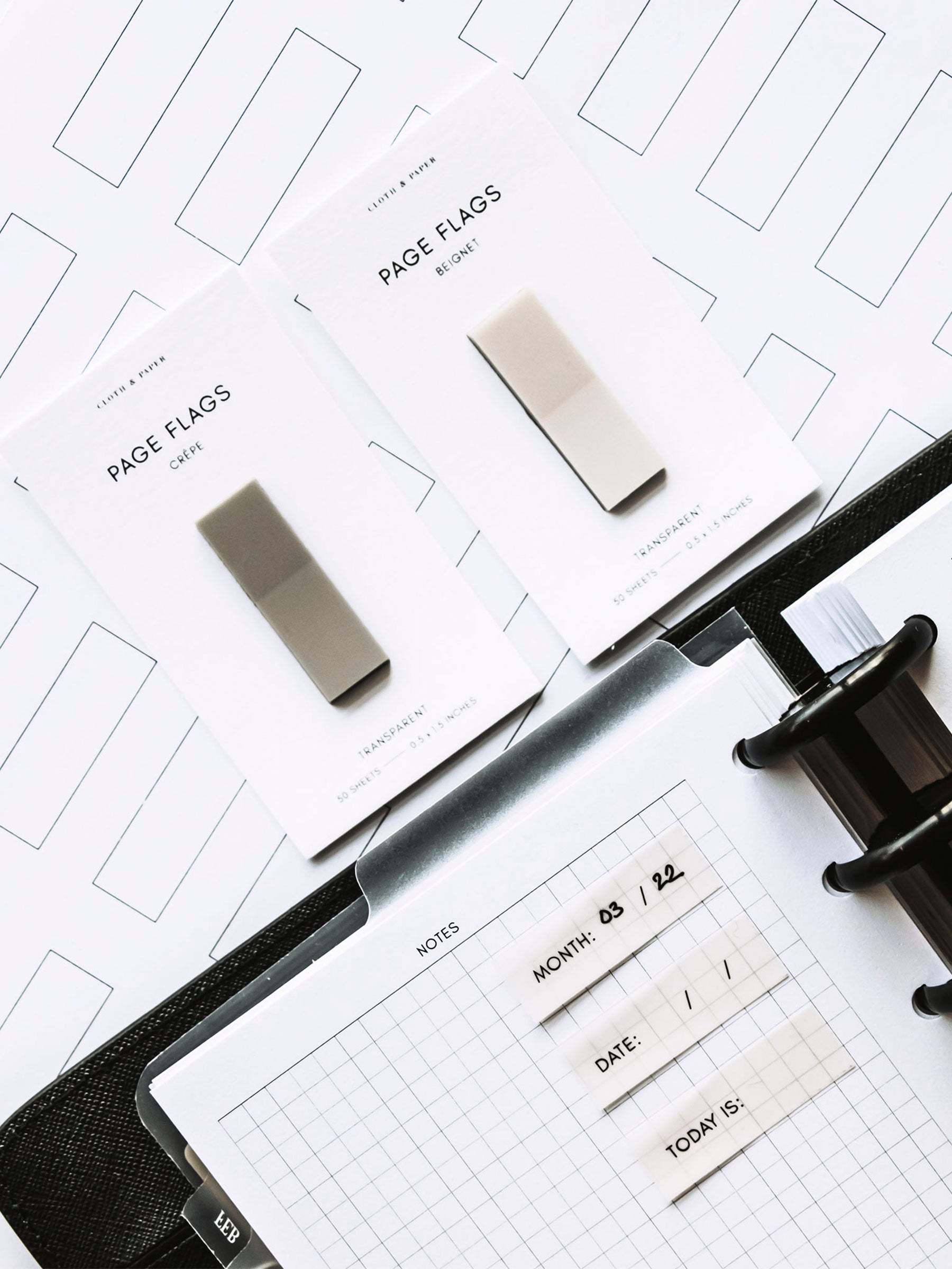 Printed page flags in use inside a discbound planner. Two pads of page flags are resting on a table next to the planner.
