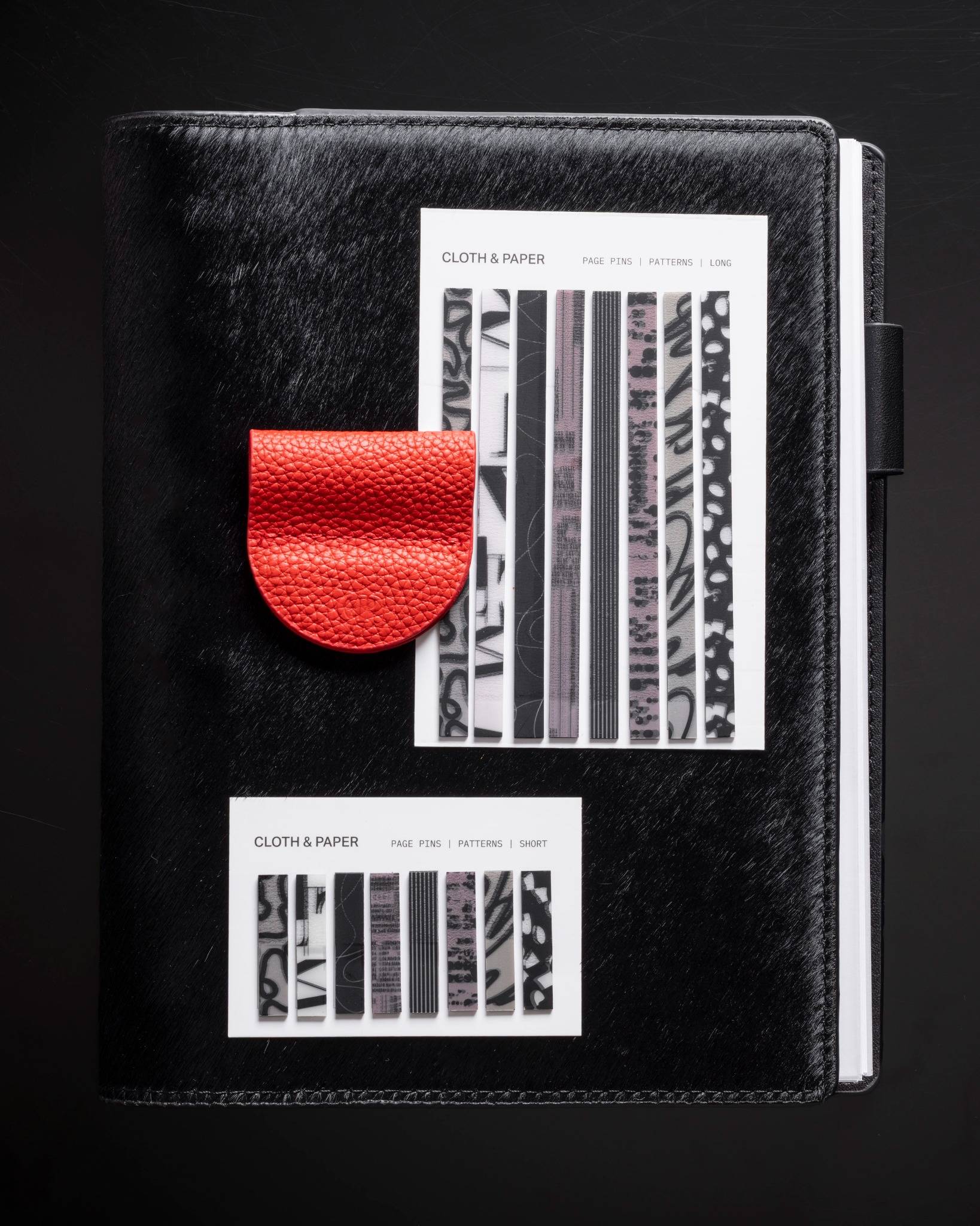Page Pins | Long and Short by Cloth & Paper displayed on a black planner with a red leather pen holder for contrast