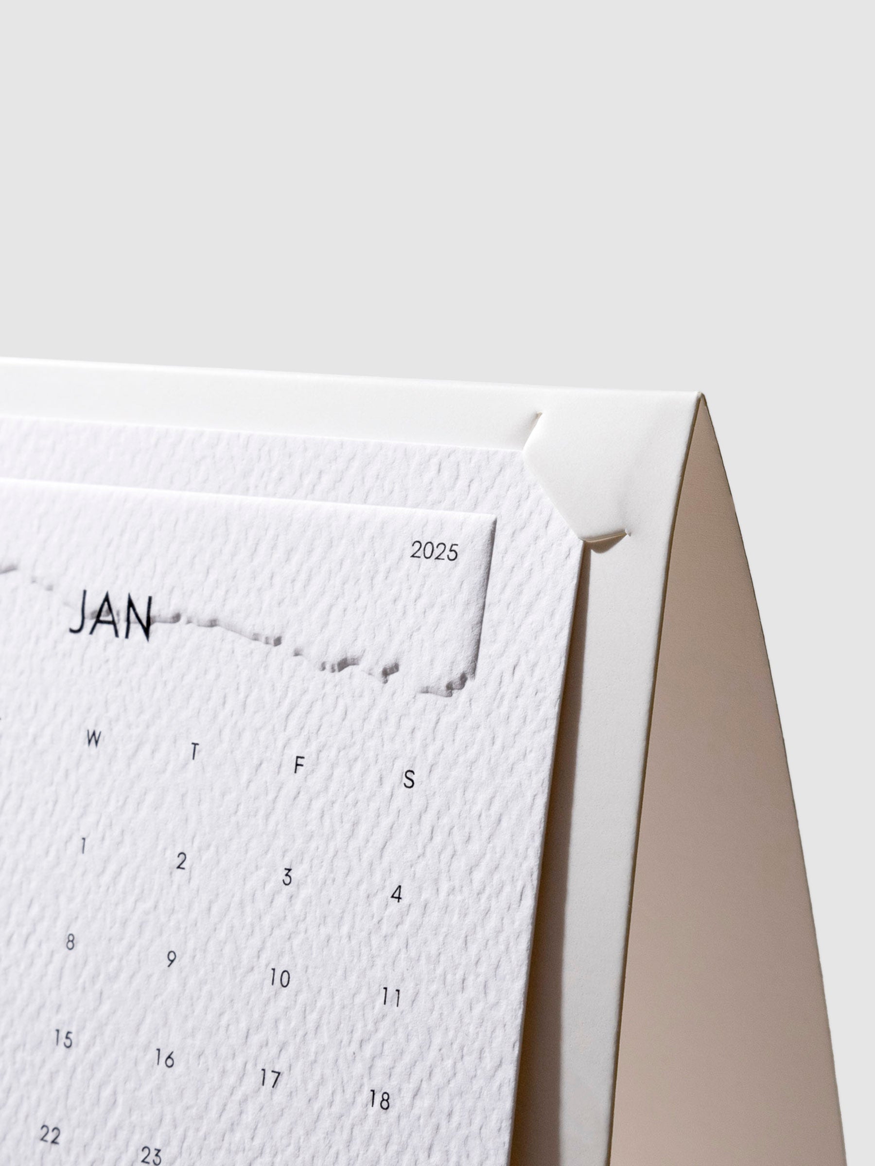 Closeup of stand shown with a 2025 calendar card fit inside of it on a neutral background.