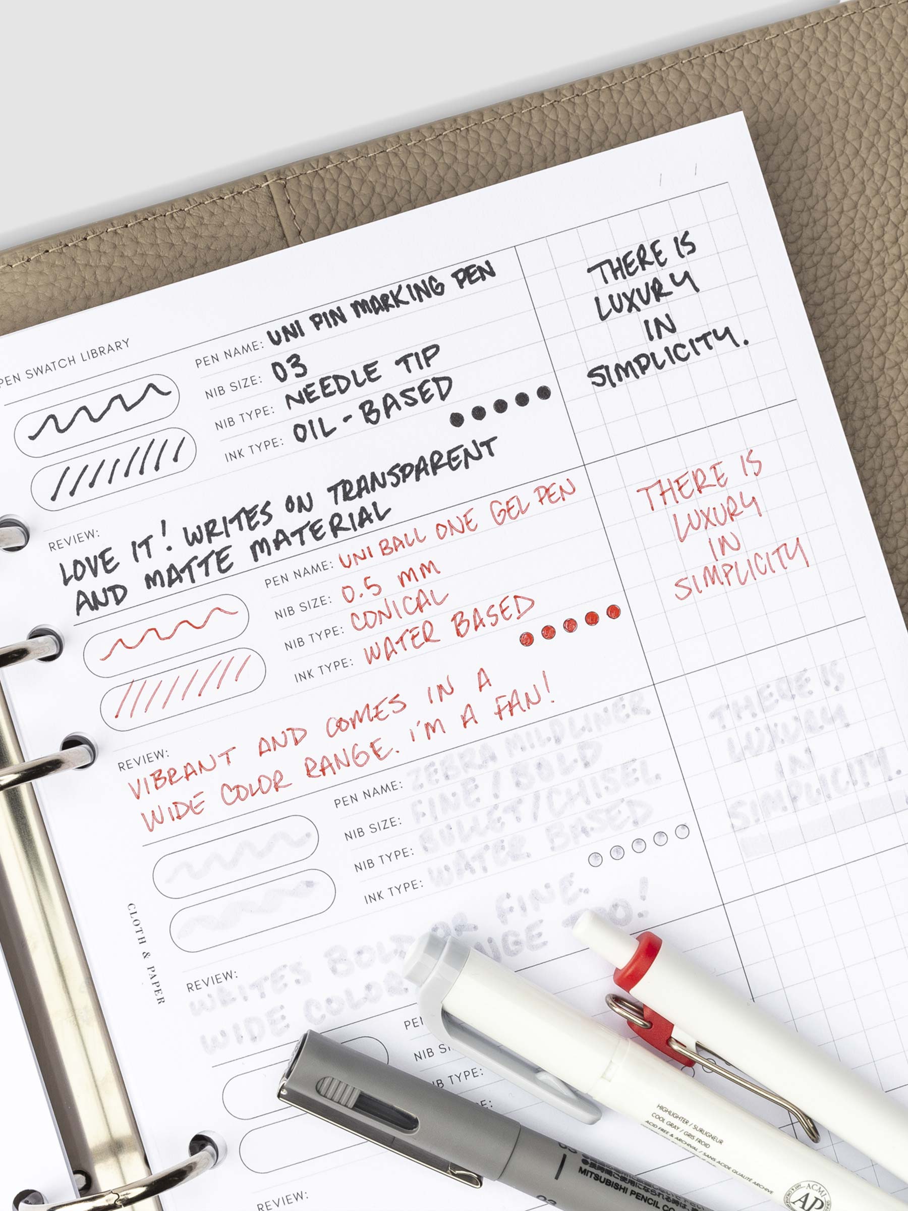 Inserts in use inside of a 6-ring binder. There are writing swatches for three pens filled out. The three pens tested are resting on the bottom of the insert.