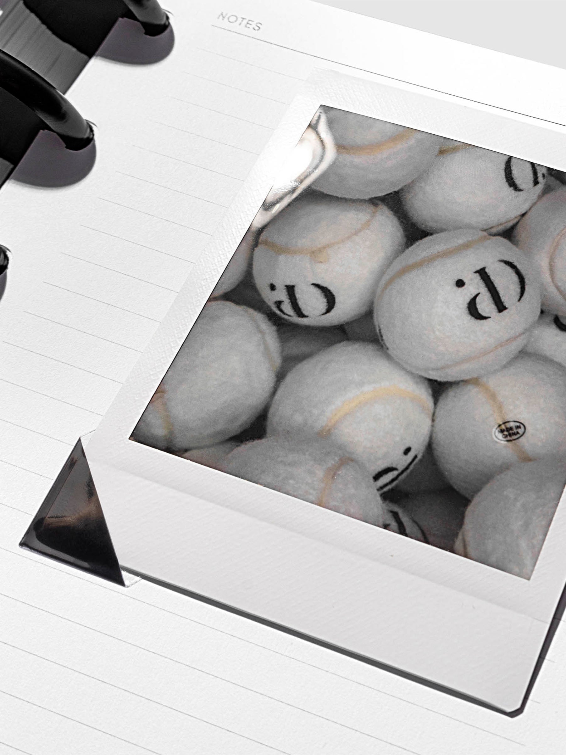 Black photo corner stickers in use, shown holding a photograph of tennis balls inside a notebook.