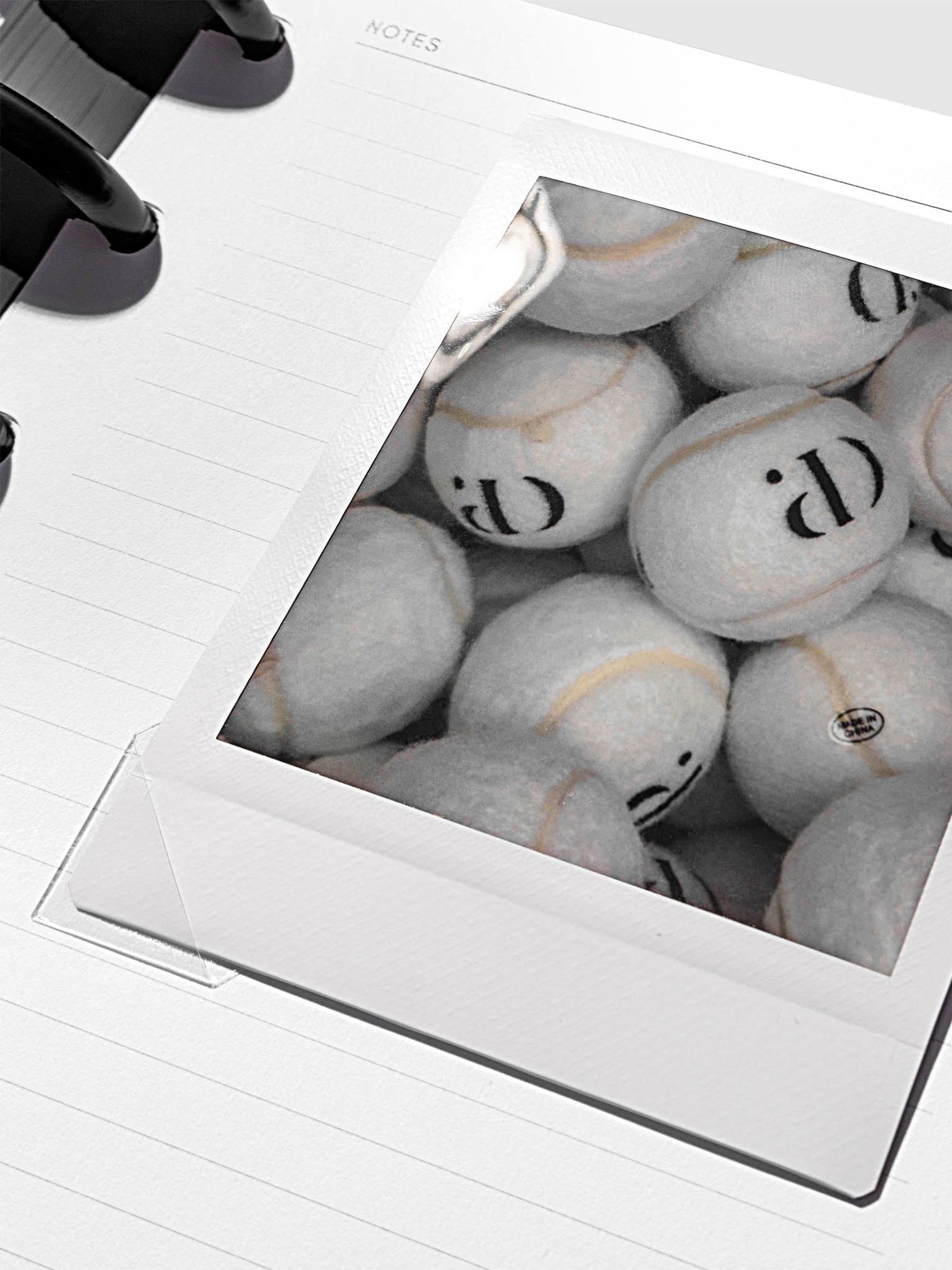 Clear photo corner stickers in use, shown holding a photograph of tennis balls inside a notebook.
