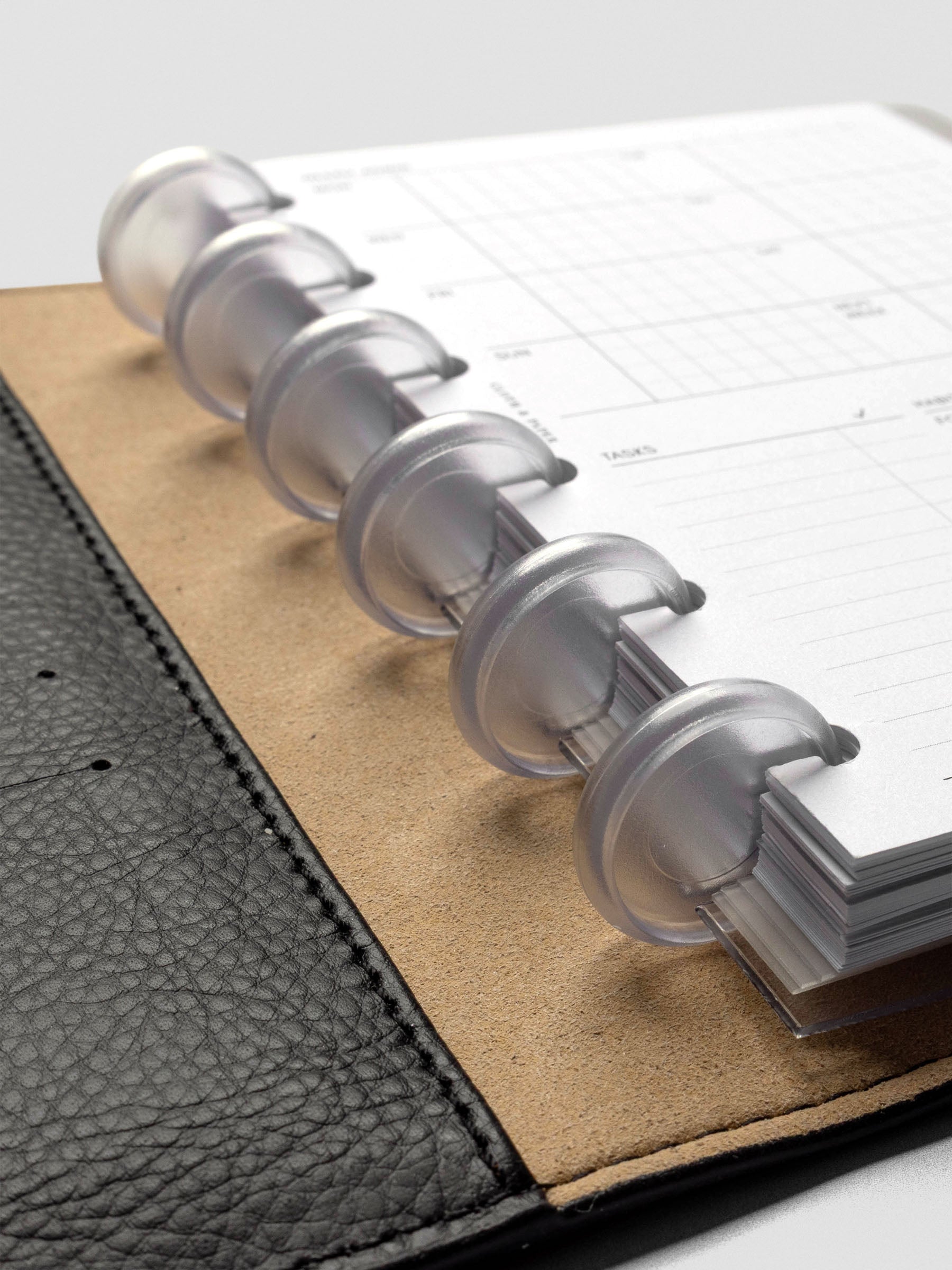 Six Clear 0.75 inch planner discs in use with CP Petite inserts and dividers in a leather folio, shown as a closeup at an angle.