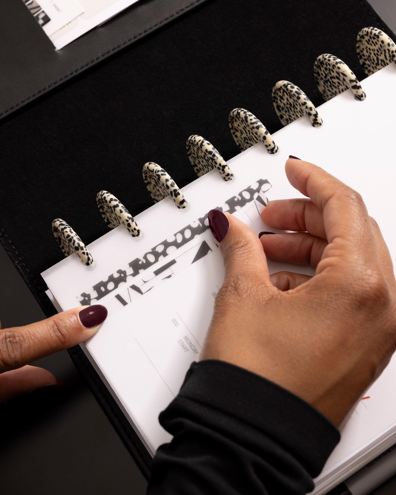 Applying a patterned page pin onto a translucent planner divider, featuring distinctive speckled planner discs.
