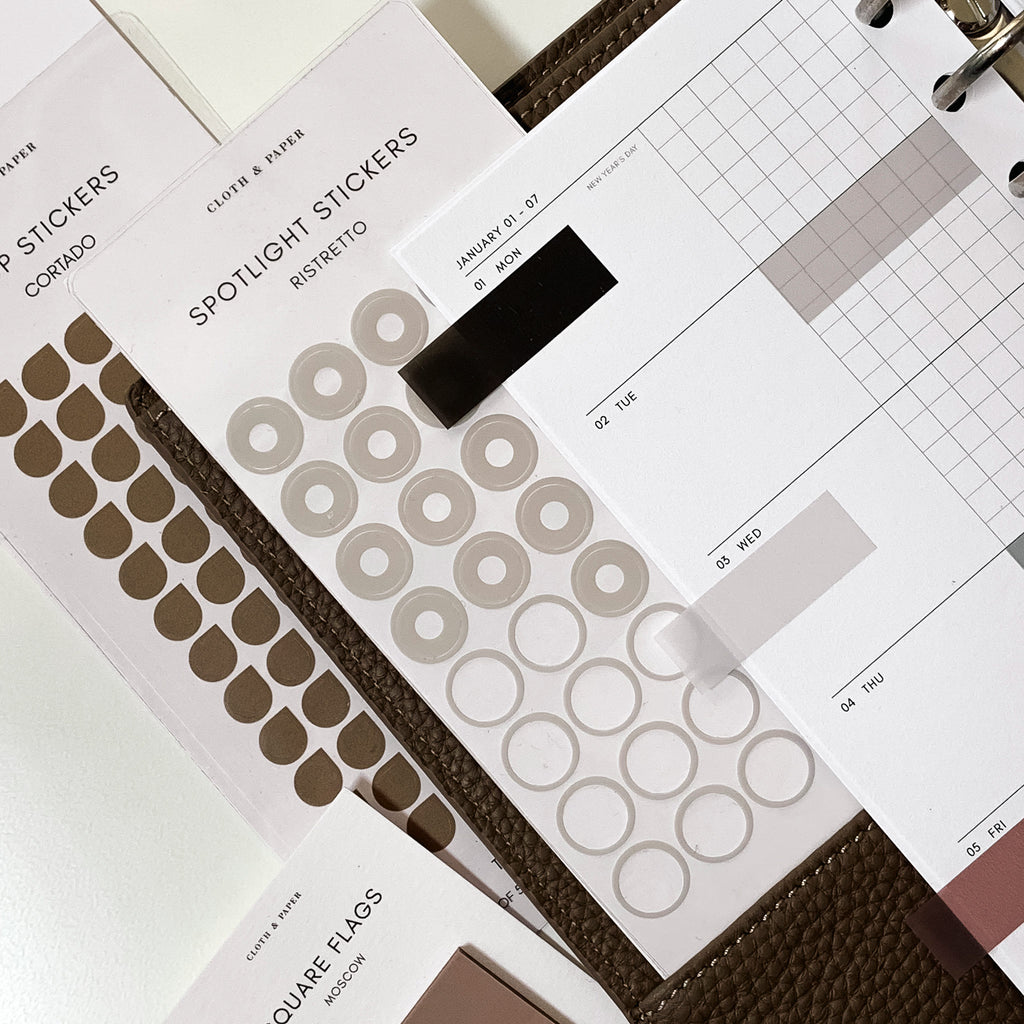 A variety of planner stickers are displayed inside a leather planner.  Inside the leather planner is a 2024 planner insert.