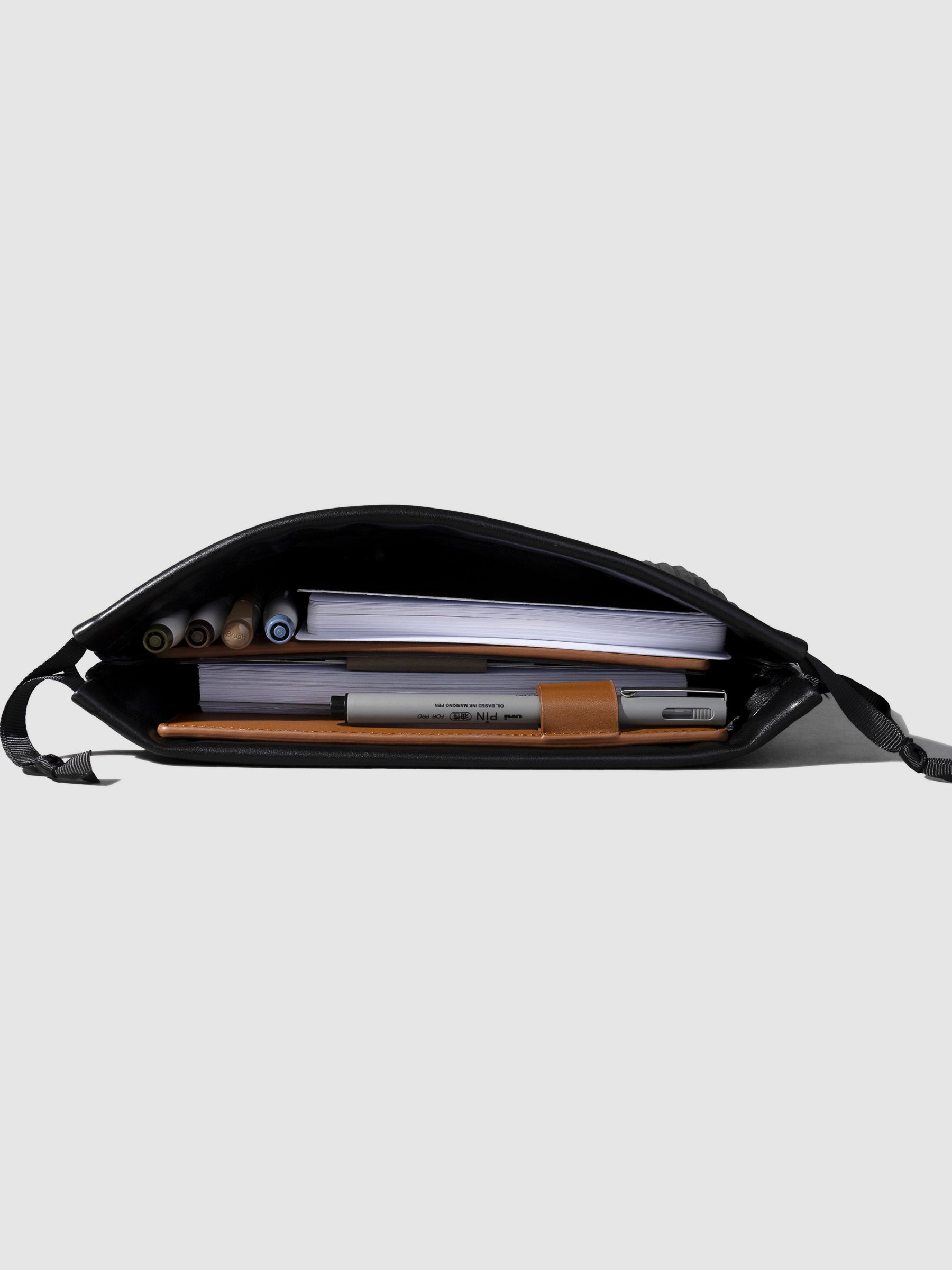 Bag displayed opened on a neutral background. Pens, notebooks, and a leather folio are stored inside.