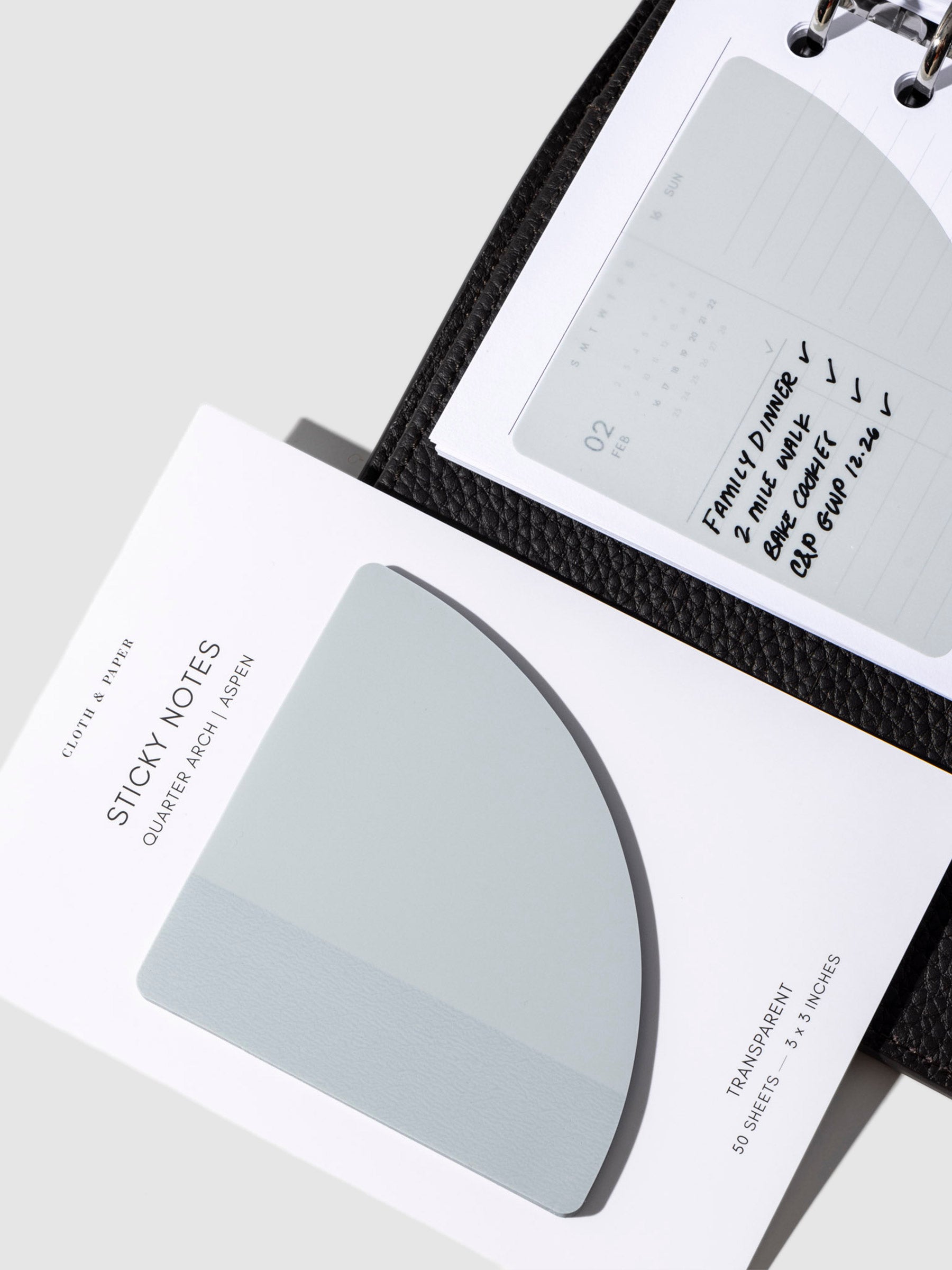 Sticky note in use inside a black leather planner. It is written on with a black oil based ink pen. The other sticky notes are displayed on top of it on their backing.