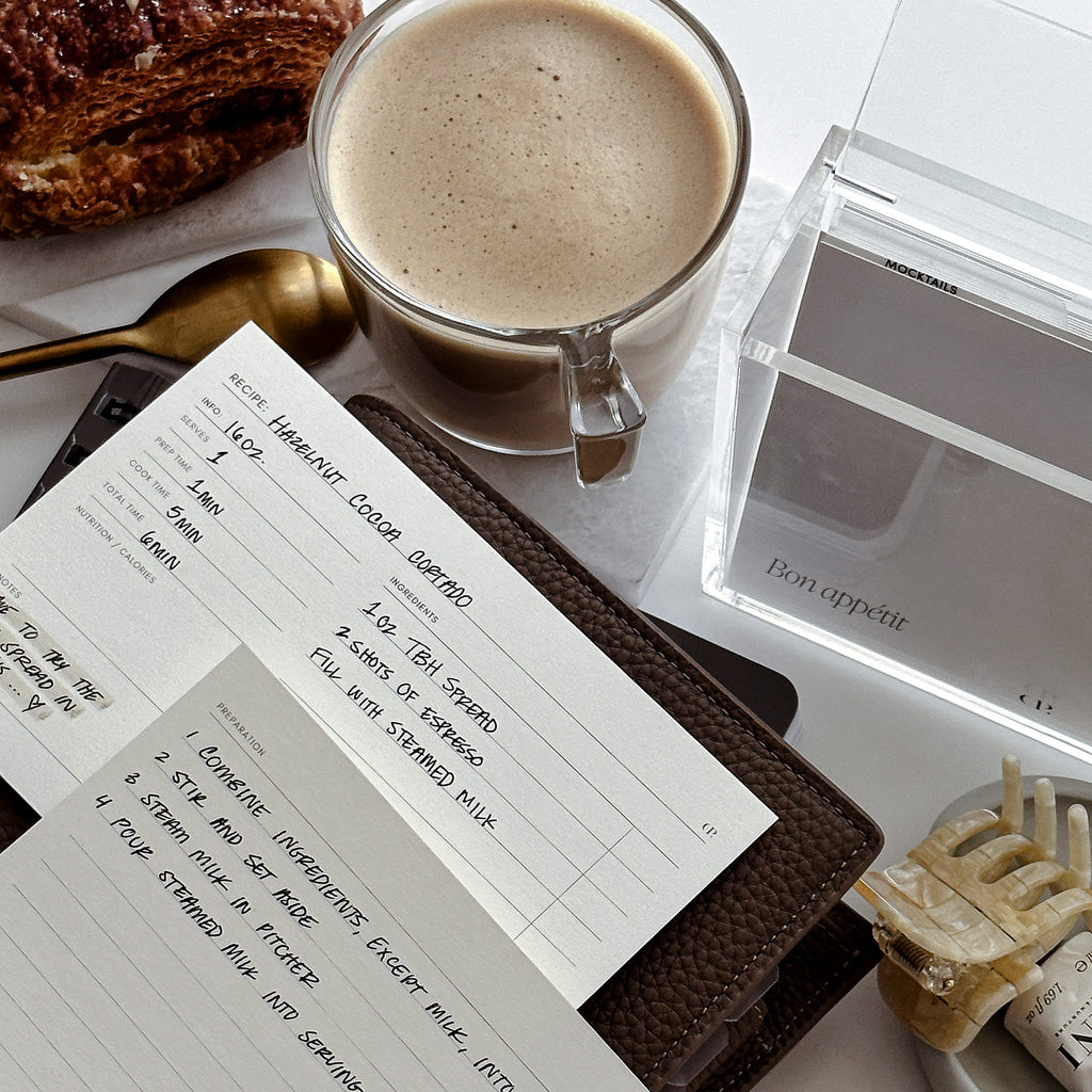 Recipe cards filled out and sitting on a leather planner.  There is a cup of coffee next to our Recipe Card Set. 