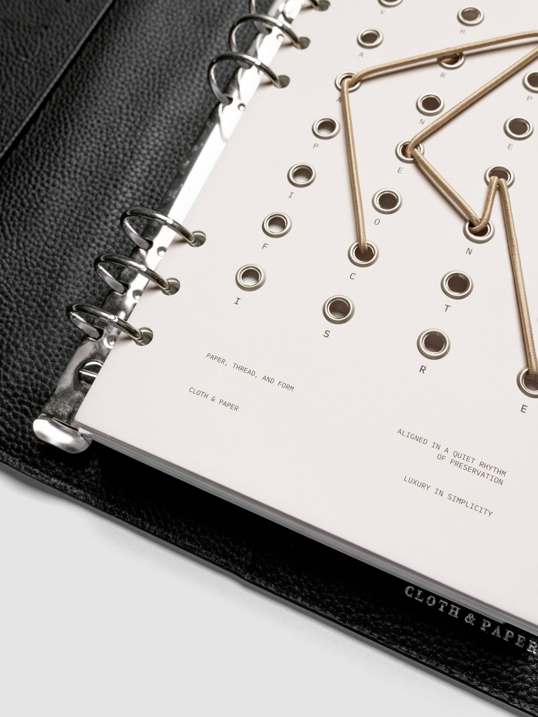 Cadence Dashboard with grommets and string on beige cardstock shown close up in a 6-ring planner.