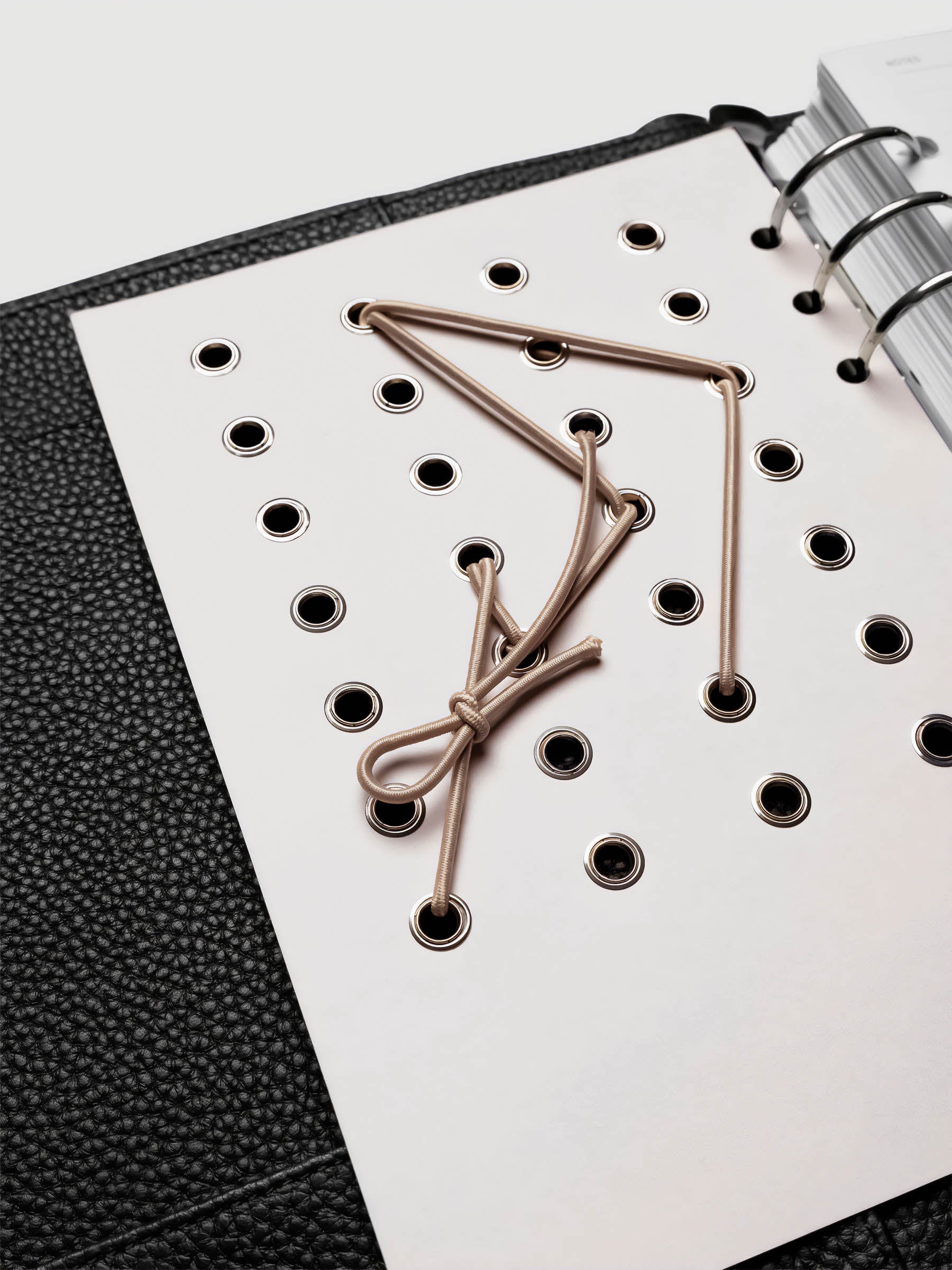 Cadence Dashboard with grommets and string on beige cardstock shown close up in a 6-ring planner.