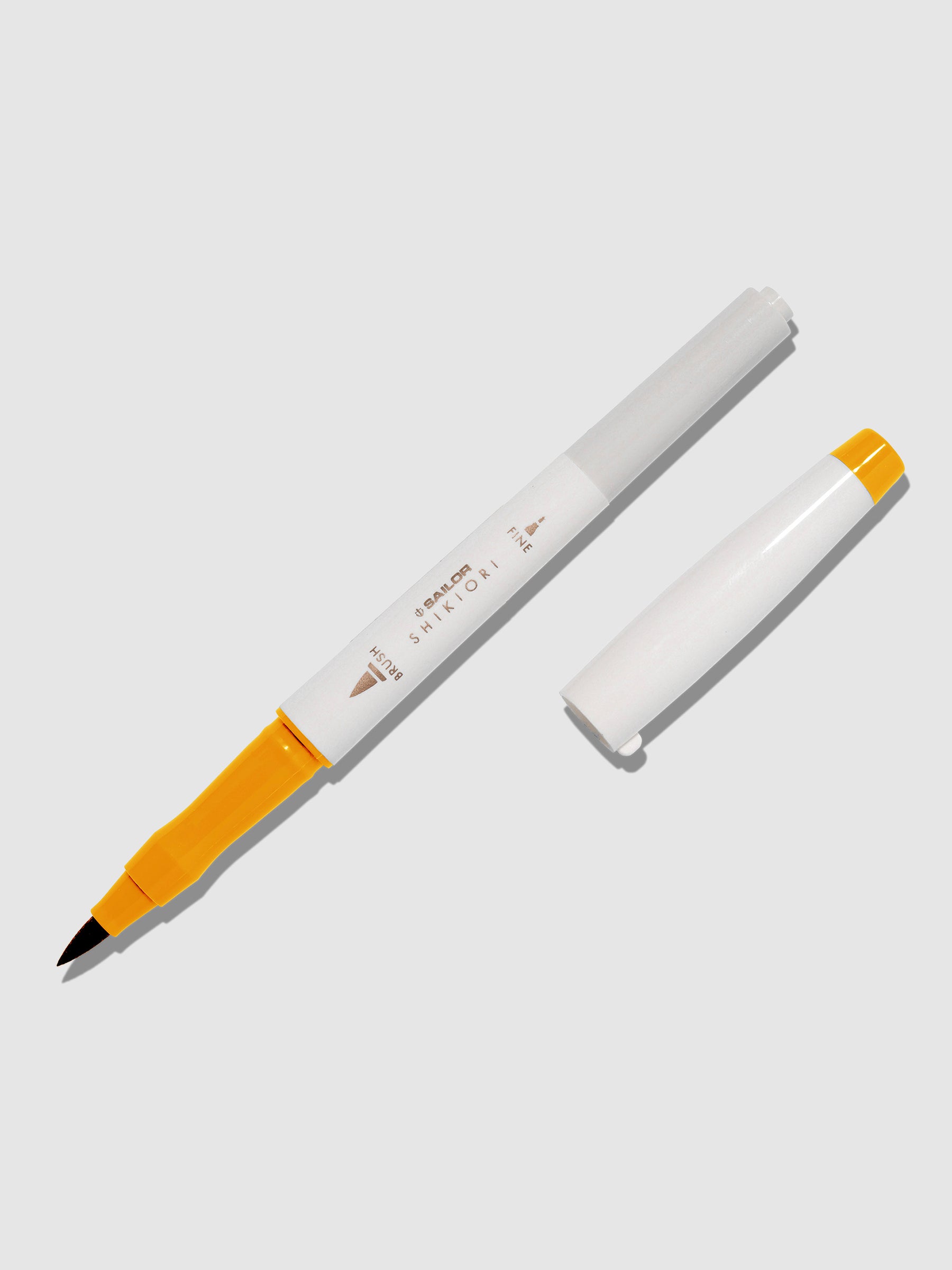 Brush pen displayed on a neutral background. It is uncapped with its brush nib exposed, and the cap lying parallel to the marker. Color pictured is Kinmokusei. 