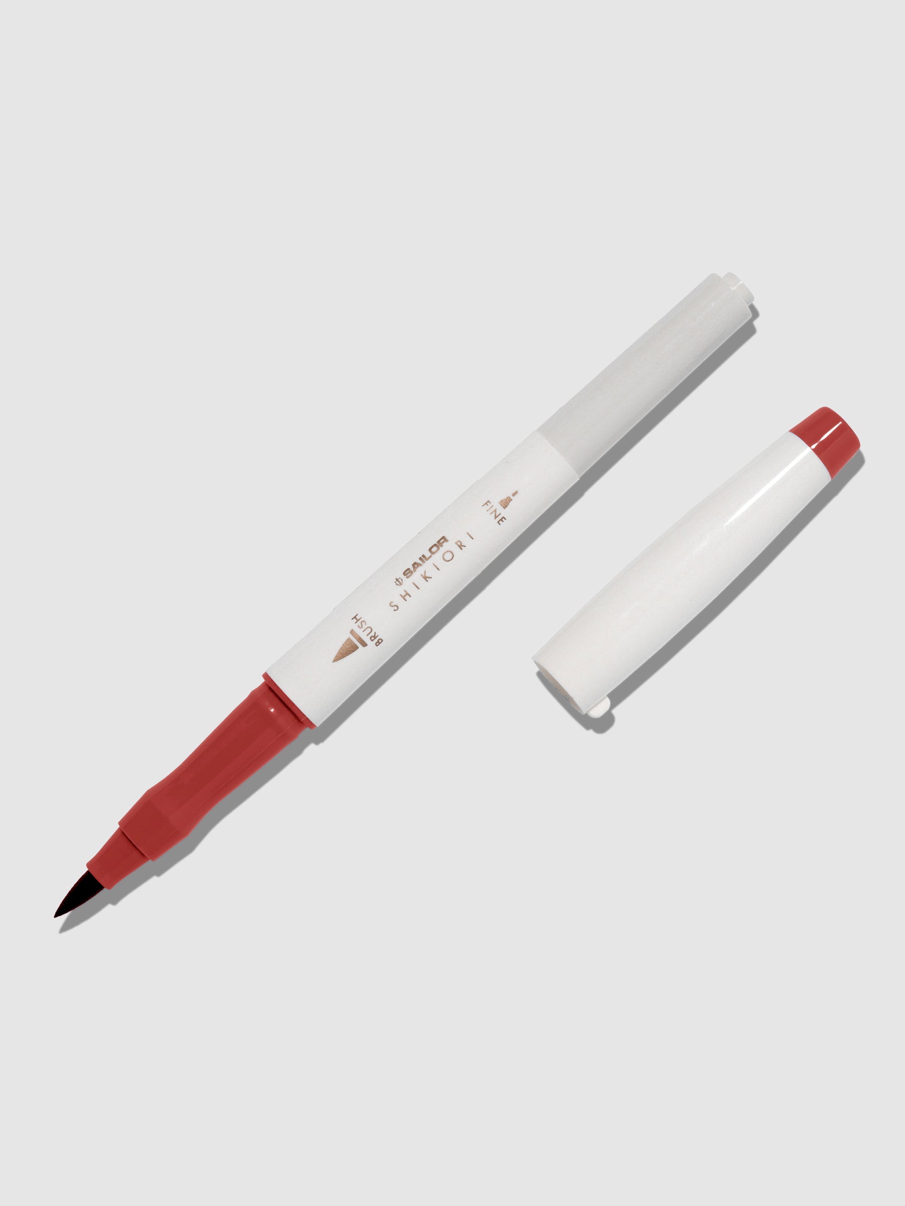 Brush pen displayed on a neutral background. It is uncapped with its brush nib exposed, and the cap lying parallel to the marker. Color pictured is Okuyama. 
