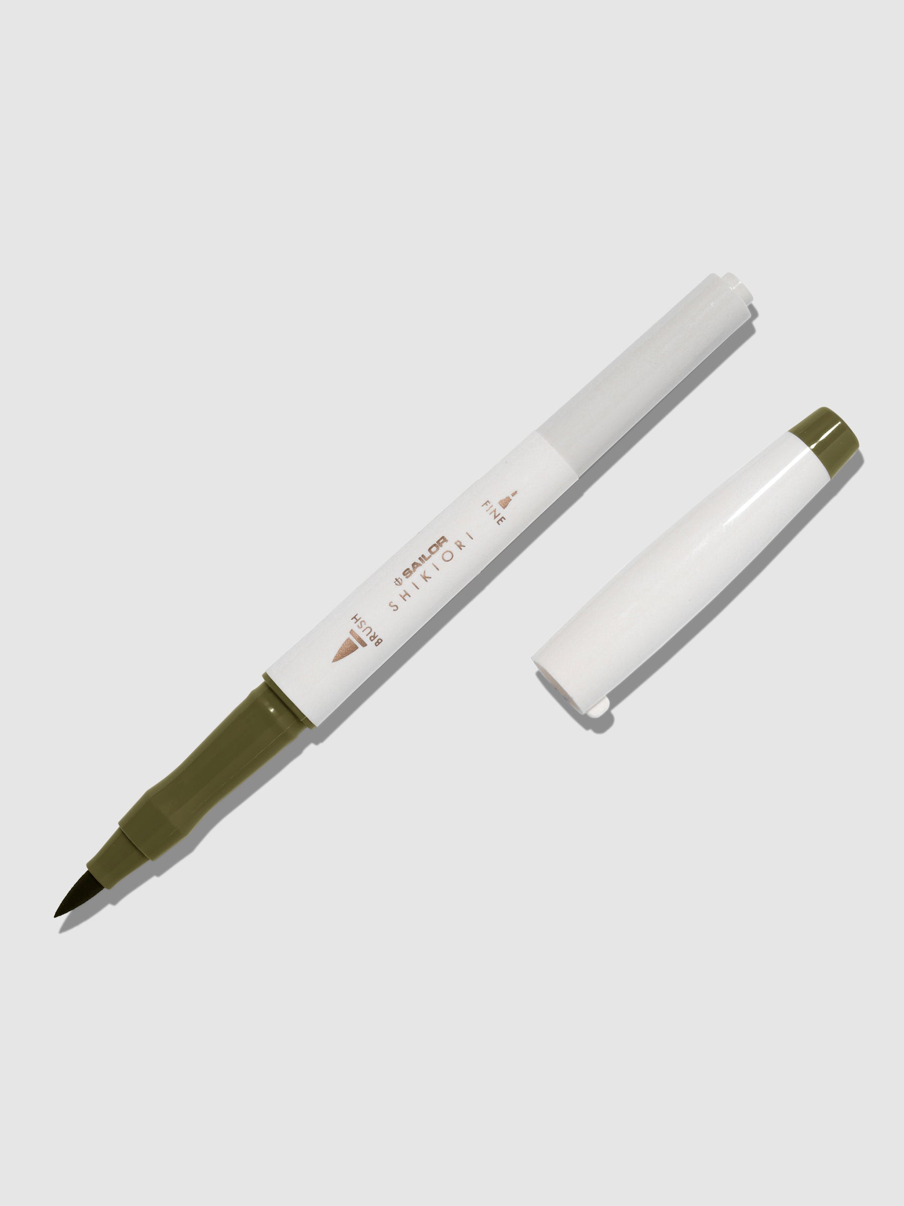 Brush pen displayed on a neutral background. It is uncapped with its brush nib exposed, and the cap lying parallel to the marker. Color pictured is Rikyucha. 
