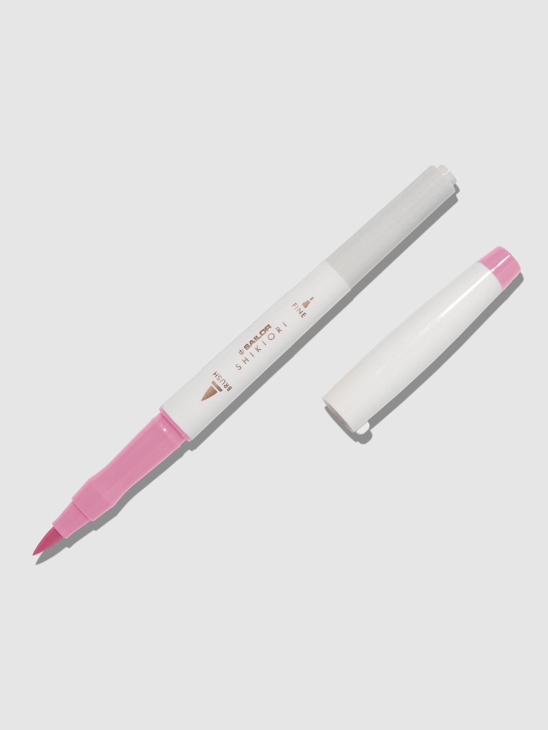 Brush pen displayed on a neutral background. It is uncapped with its brush nib exposed, and the cap lying parallel to the marker. Color pictured is Sakuramori. 