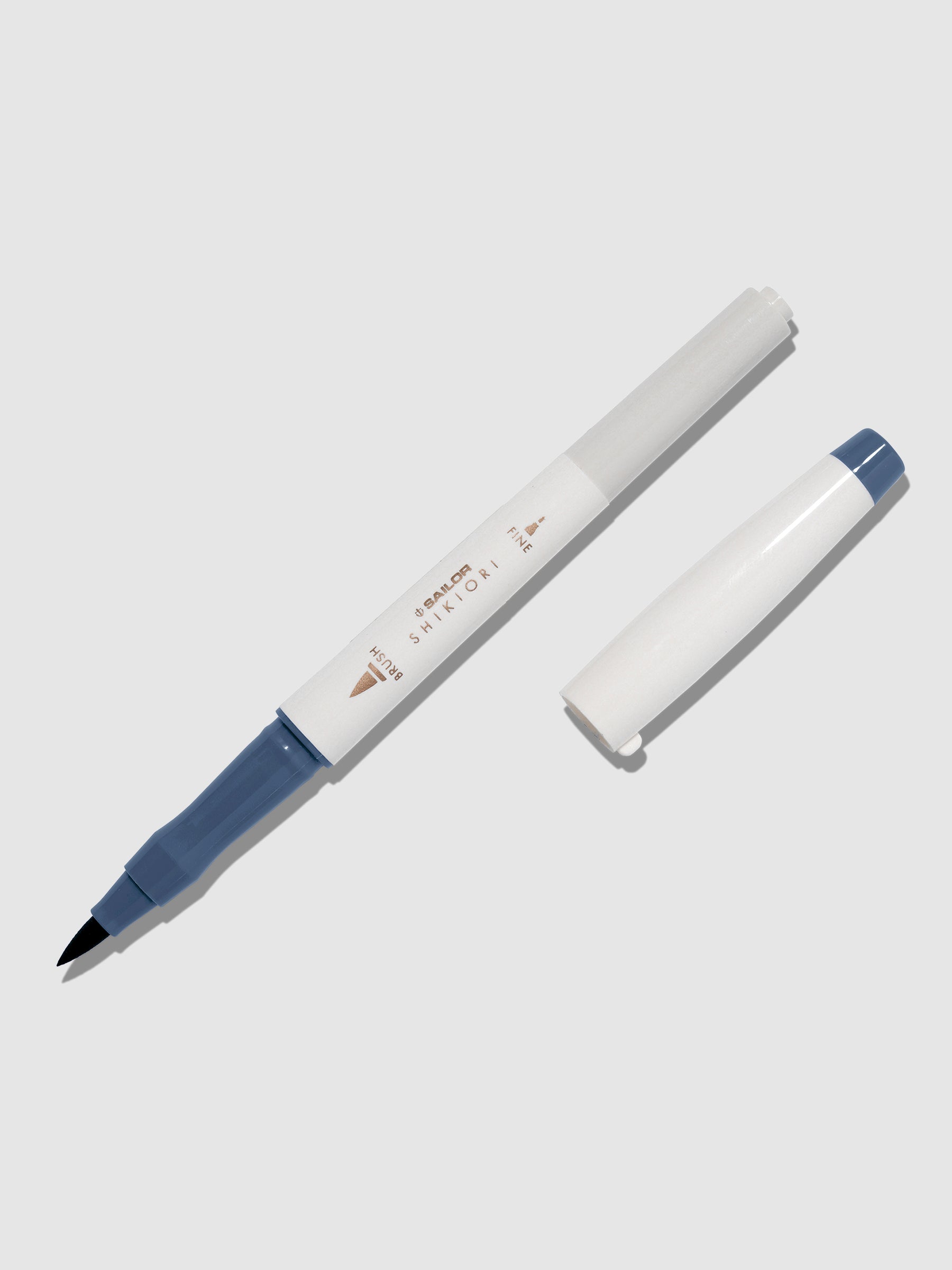 Brush pen displayed on a neutral background. It is uncapped with its brush nib exposed, and the cap lying parallel to the marker. Color pictured is Shimoyo. 