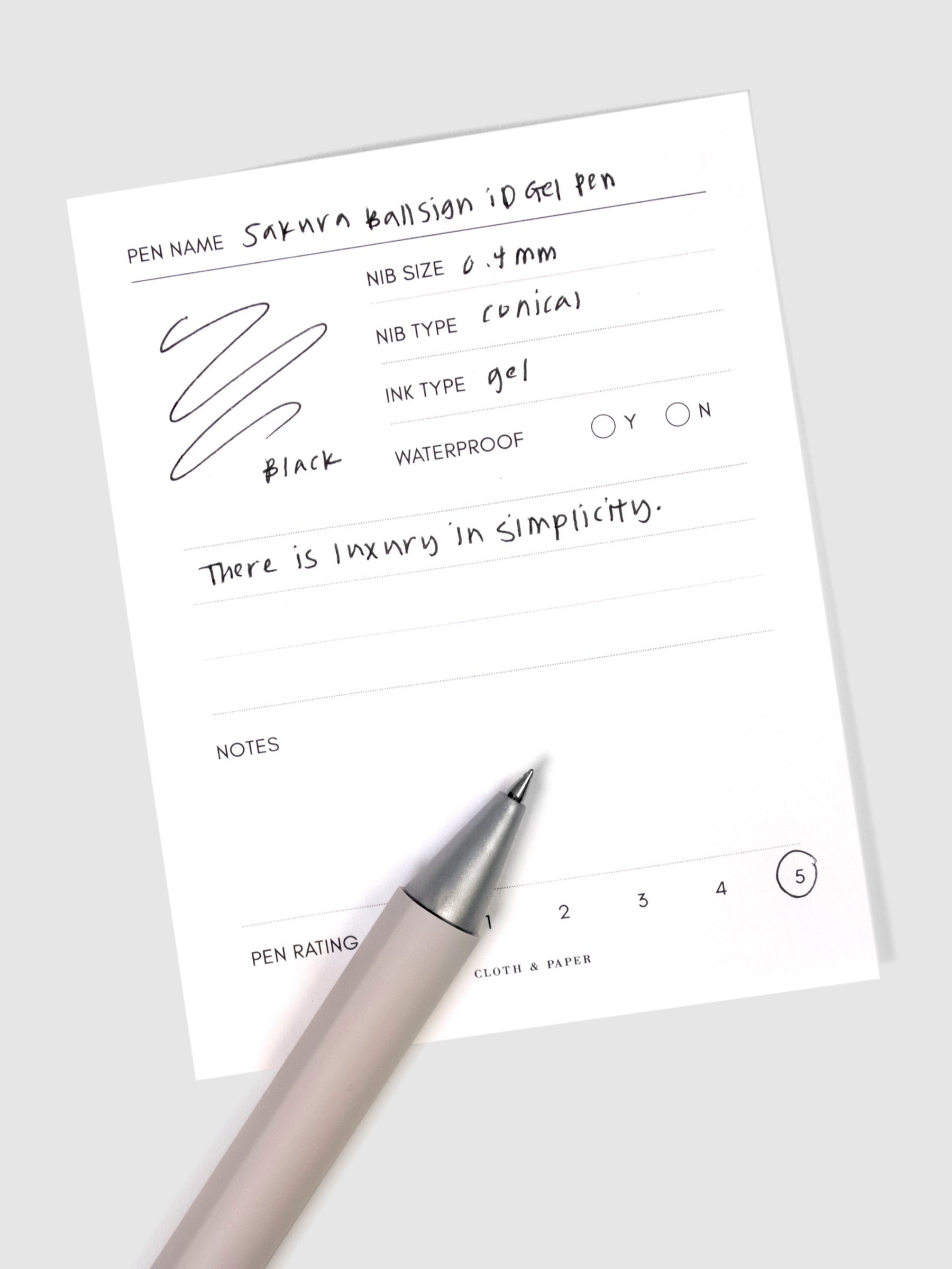Sakura Ballsign iD Gel Pen, 0.4 mm, Cloth and Paper. Black pen resting on pen test sheet displaying writing sample.