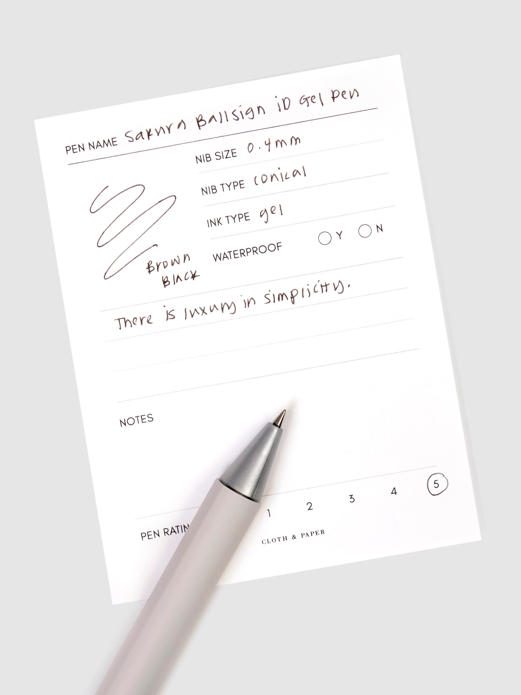 Sakura Ballsign iD Gel Pen, 0.4 mm, Cloth and Paper. Brown black pen resting on pen test sheet displaying writing sample.