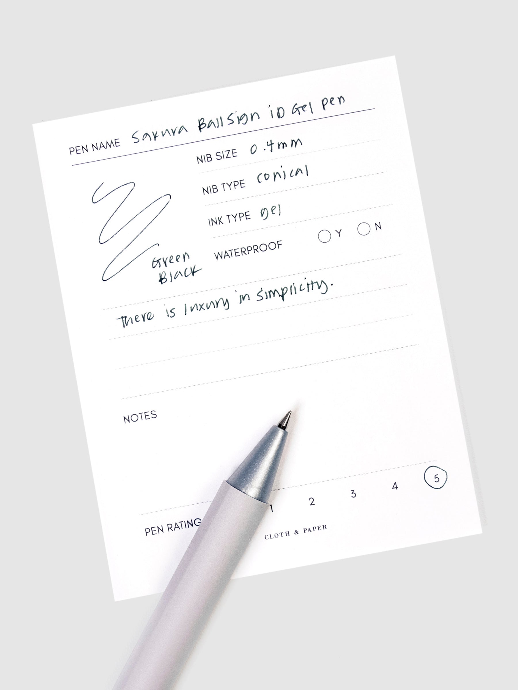 Sakura Ballsign iD Gel Pen, 0.4 mm, Cloth and Paper. Green black pen resting on pen test sheet displaying writing sample.