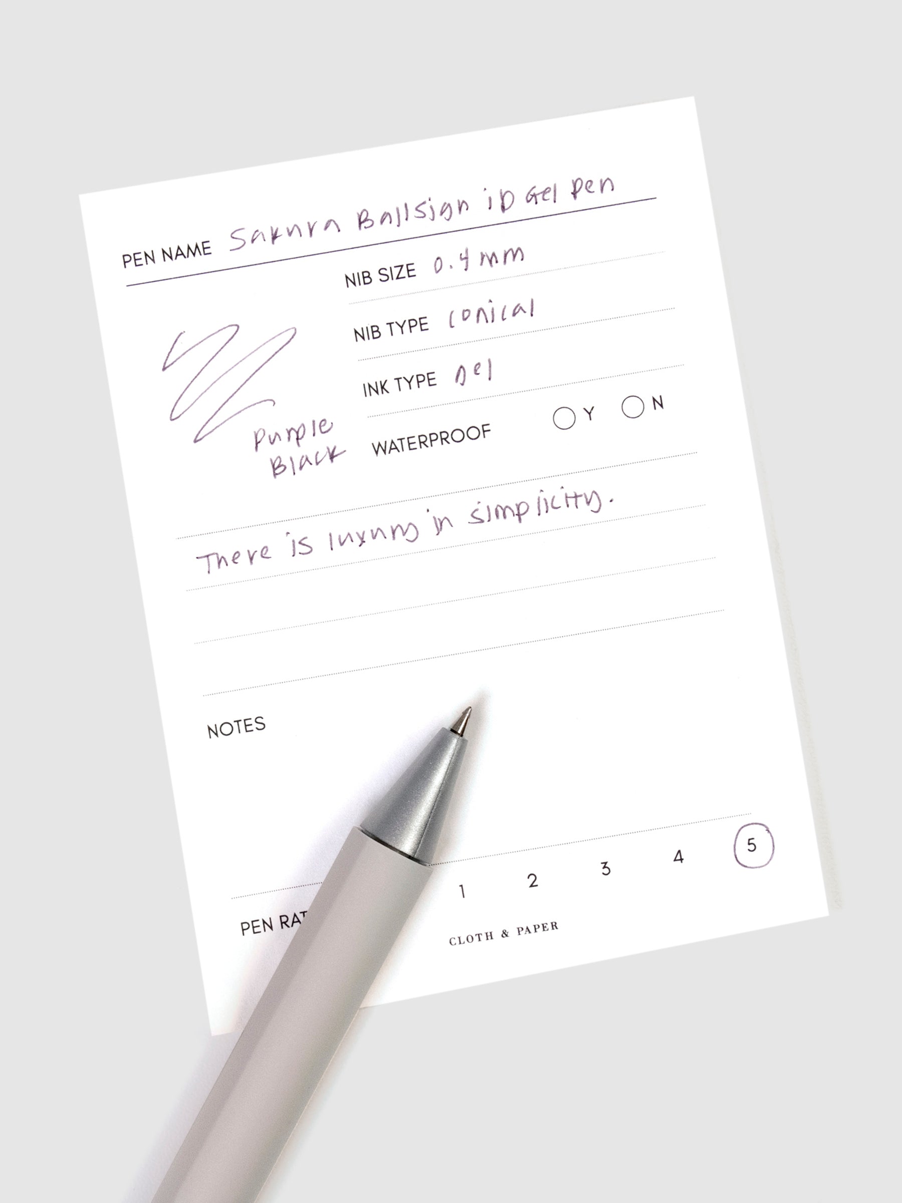 Sakura Ballsign iD Gel Pen, 0.4 mm, Cloth and Paper. Purple black pen resting on pen test sheet displaying writing sample.