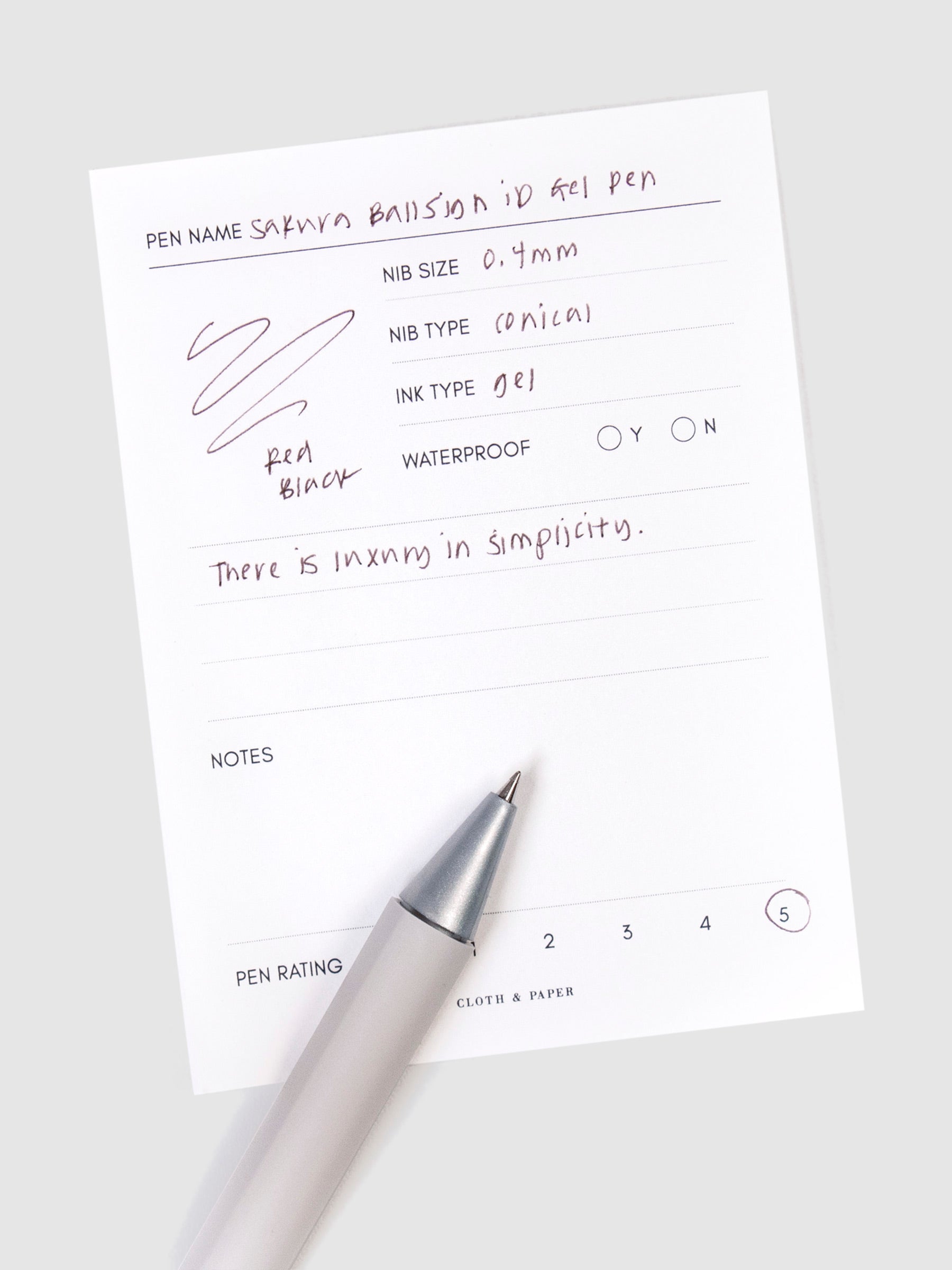 Sakura Ballsign iD Gel Pen, 0.4 mm, Cloth and Paper. Red black pen resting on pen test sheet displaying writing sample.