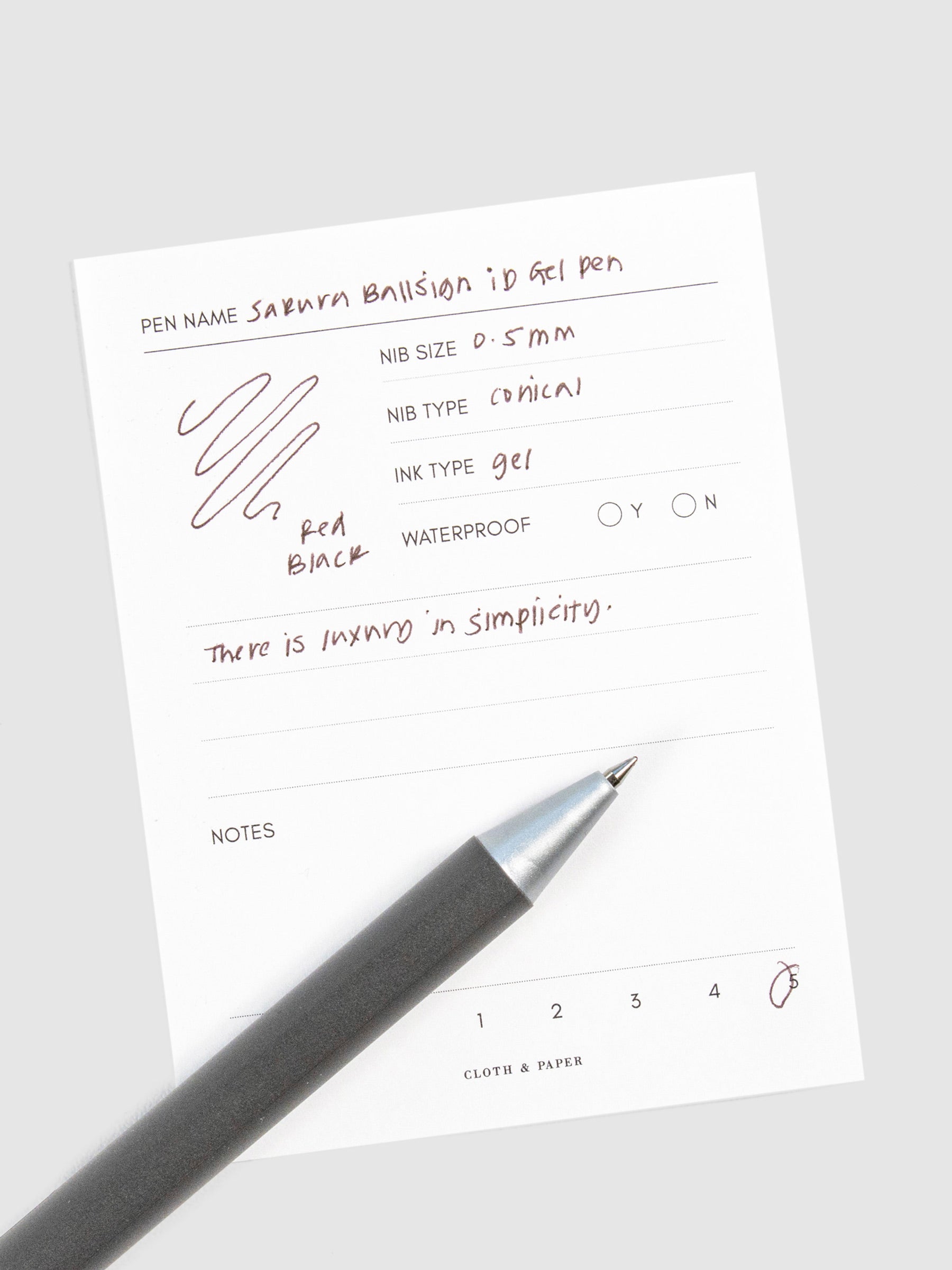 Pen in Red Black resting on a pen test sheet displaying a writing sample detailing the pen's specs.