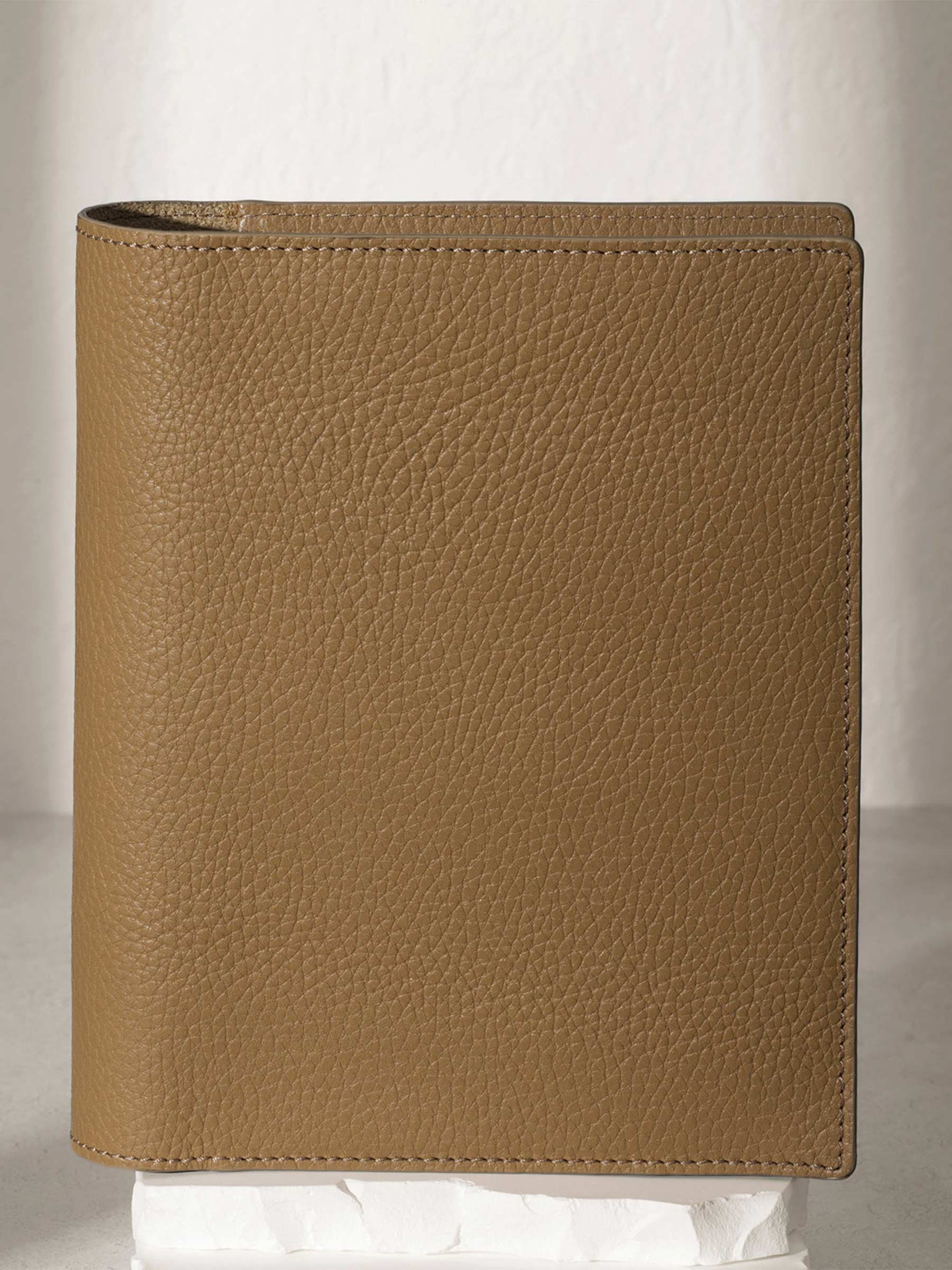 Small Catalonia folio displayed on a white stone pedestal. The background is a natural textured off-white material, and a spotlight behind the folio highlights its placement.