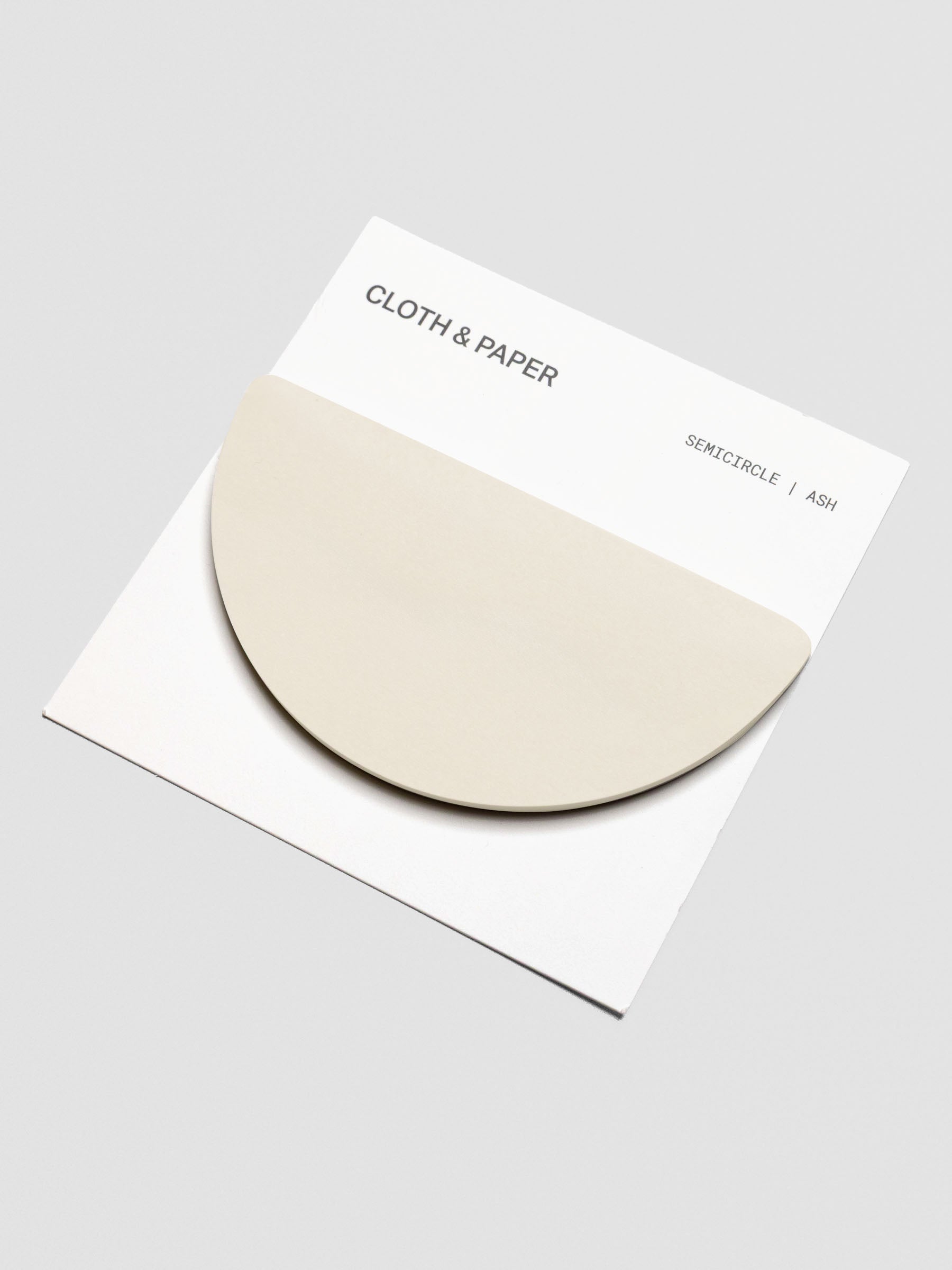 Angled view of Cloth & Paper Semicircle Sticky Notes in Ash. The pale beige half-circle pad is mounted on a white backing card with simple black text.