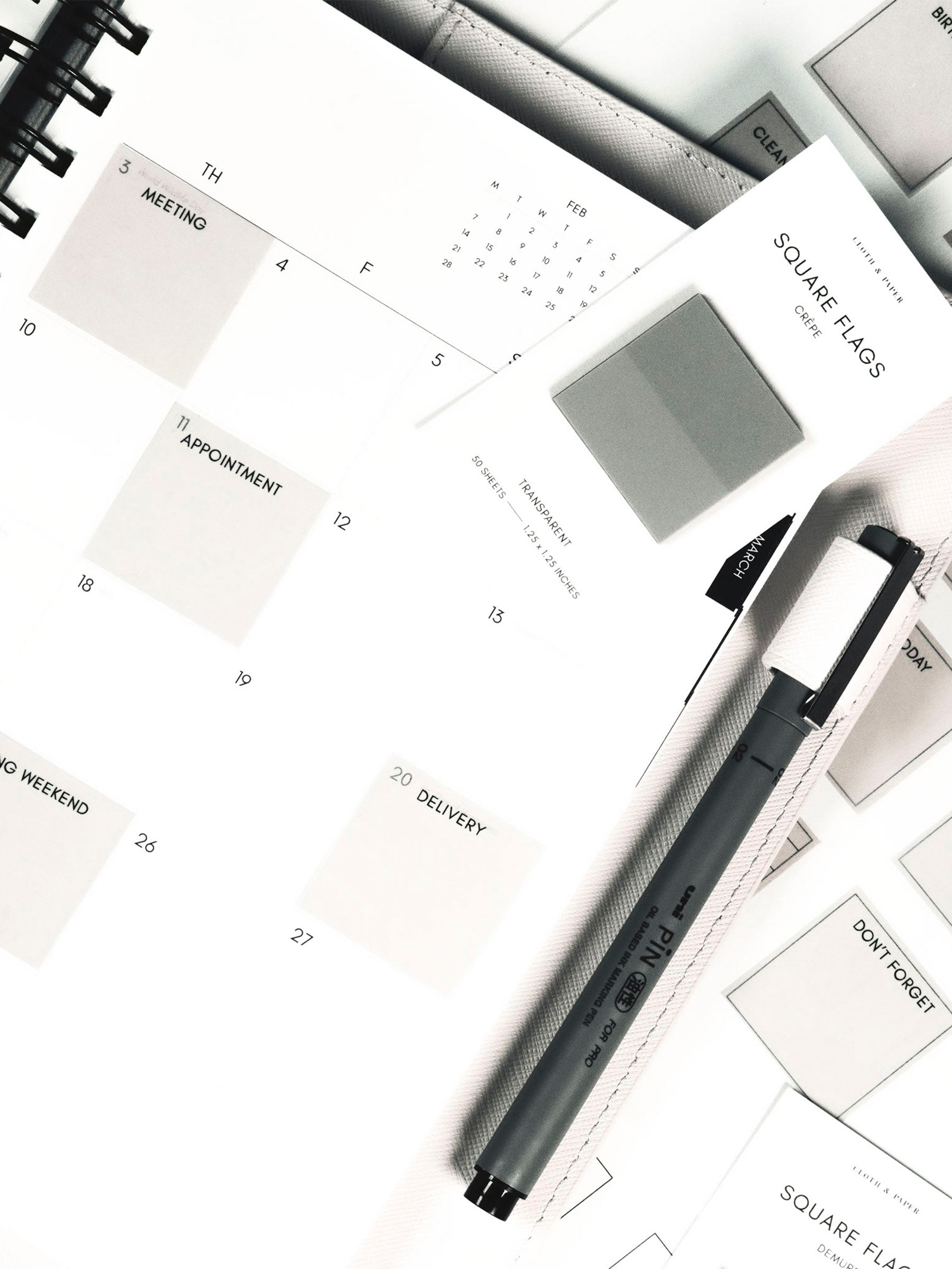 Square Page Flag Printable | Essentials page layered under a planner showing page flags in use. A Uni Pin Marking Pen is in the planner's pen loop and a set of square page flags are resting on top of the planner.