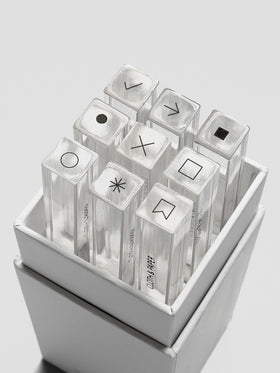 Open box revealing nine clear acrylic stamp sticks neatly arranged inside, each topped with a black icon.