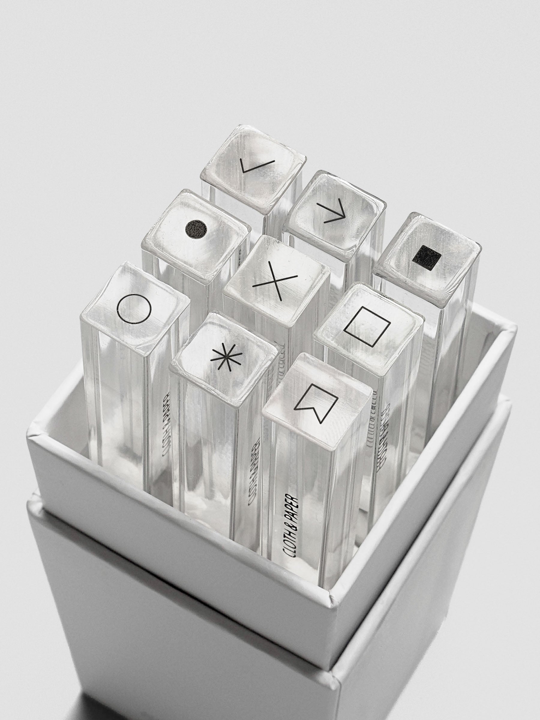 Open box revealing nine clear acrylic stamp sticks neatly arranged inside, each topped with a black icon.