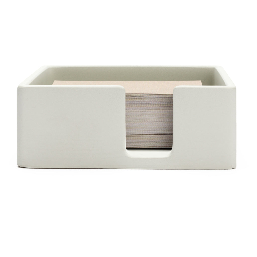 Sticky note holder facing forward on a white background. The sticky note holder contains a large amount of sticky notes, filling it to the container's brim.