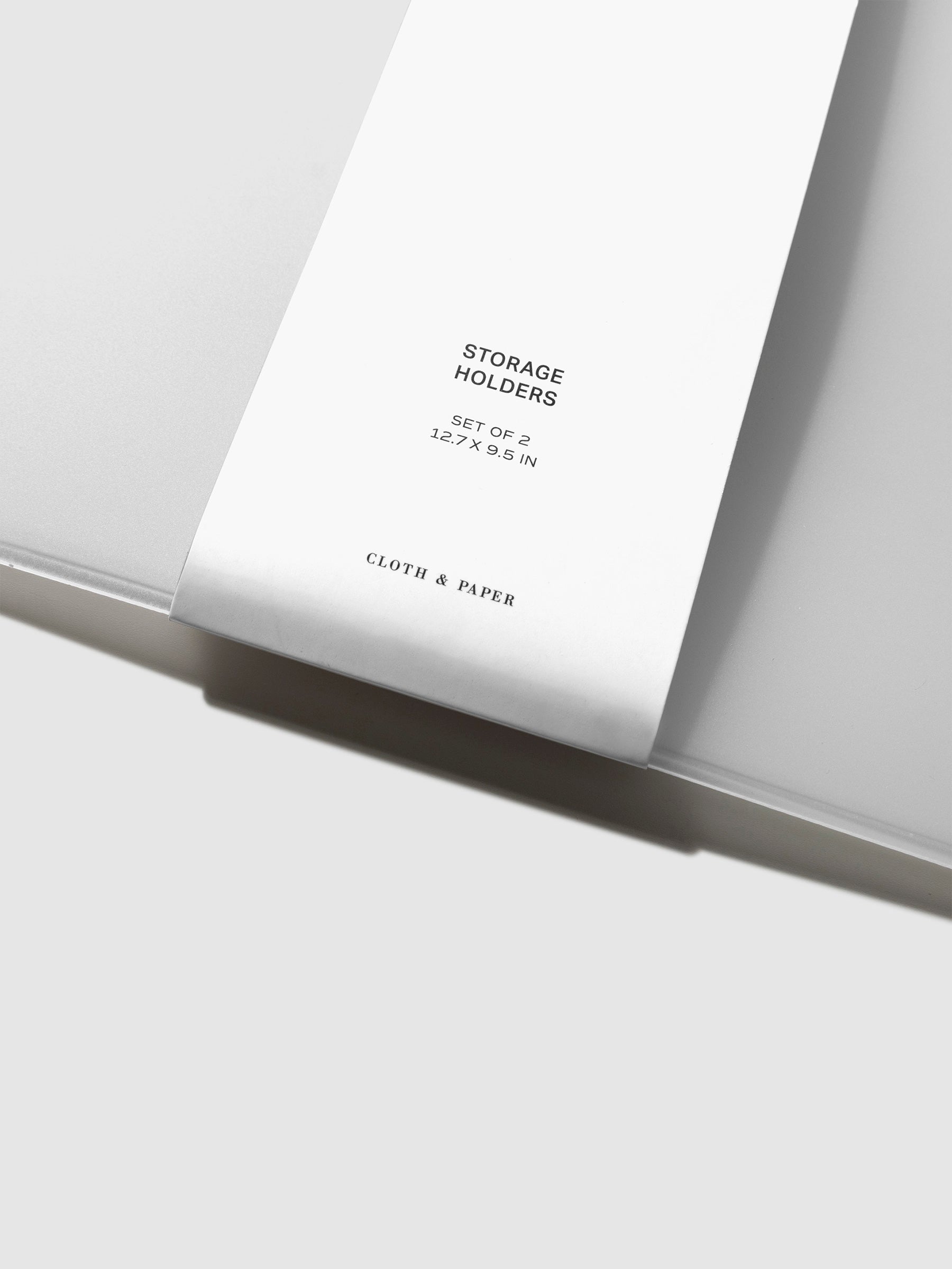 Closeup of packaging for storage holder. Text reads "STORAGE HOLDERS | SET OF 2 | 12.7 X 9.5 INCHES | CLOTH & PAPER"